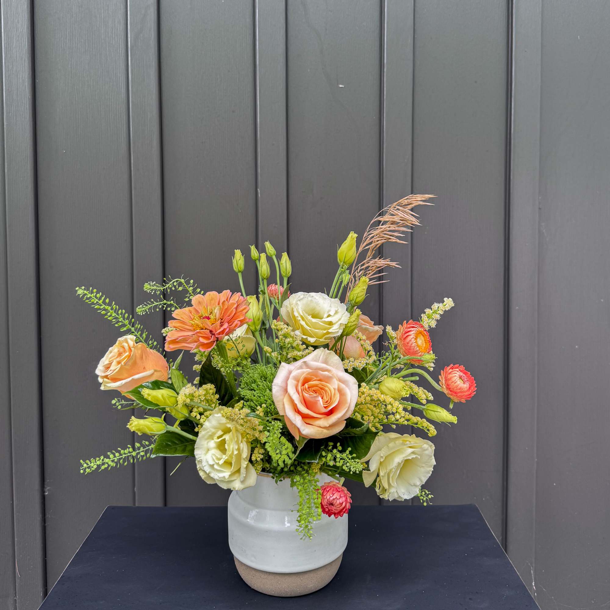 Mixed bouquet of peach, cream, and orange flowers in a white ceramic vase