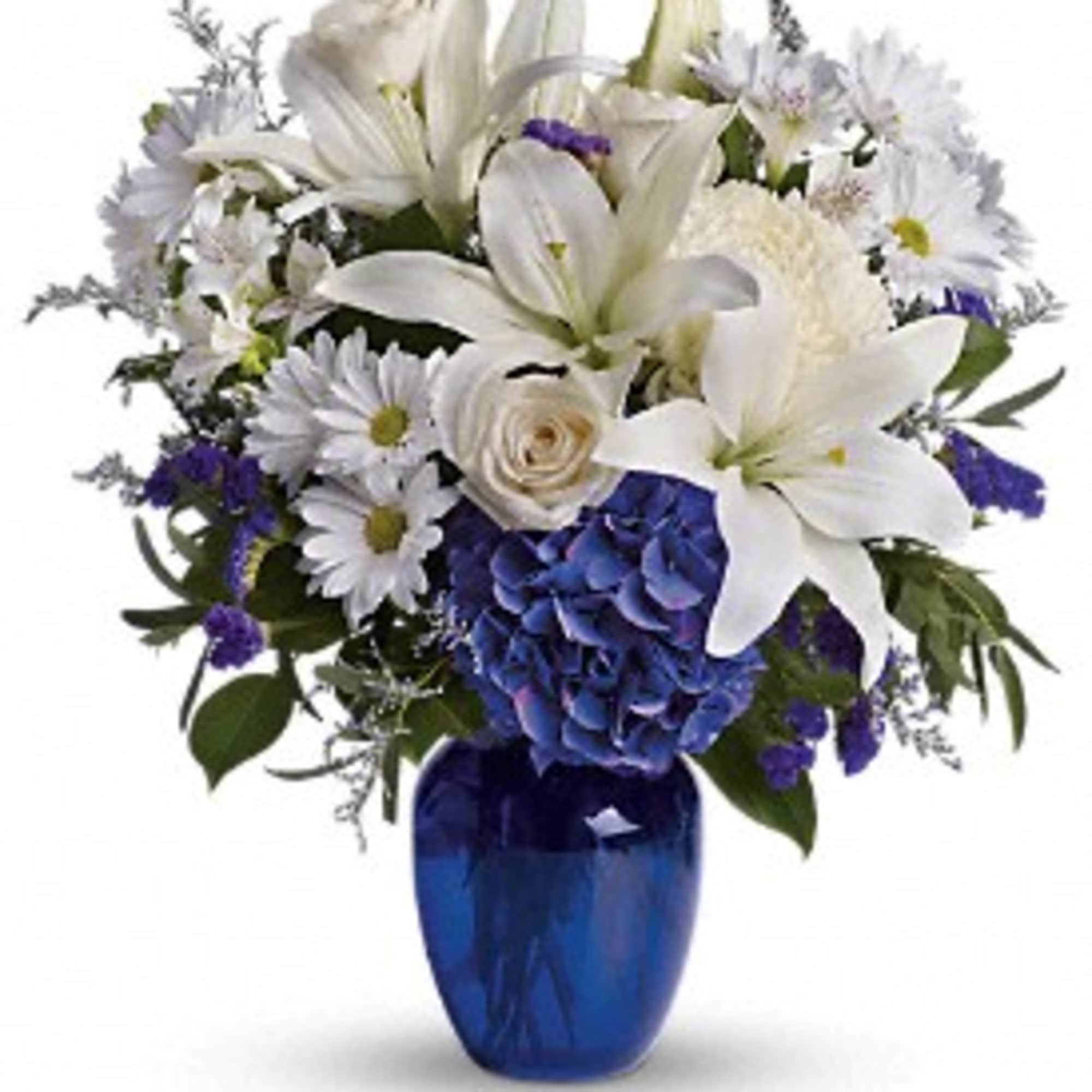 White lilies, daisies and blue hydrangeas arranged in a cobalt blue glass vase