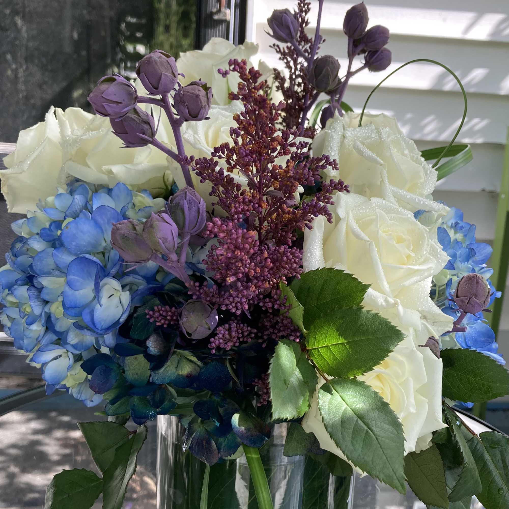 White roses and blue hydrangeas in a glass vase with purple accents, photo 3 of 4