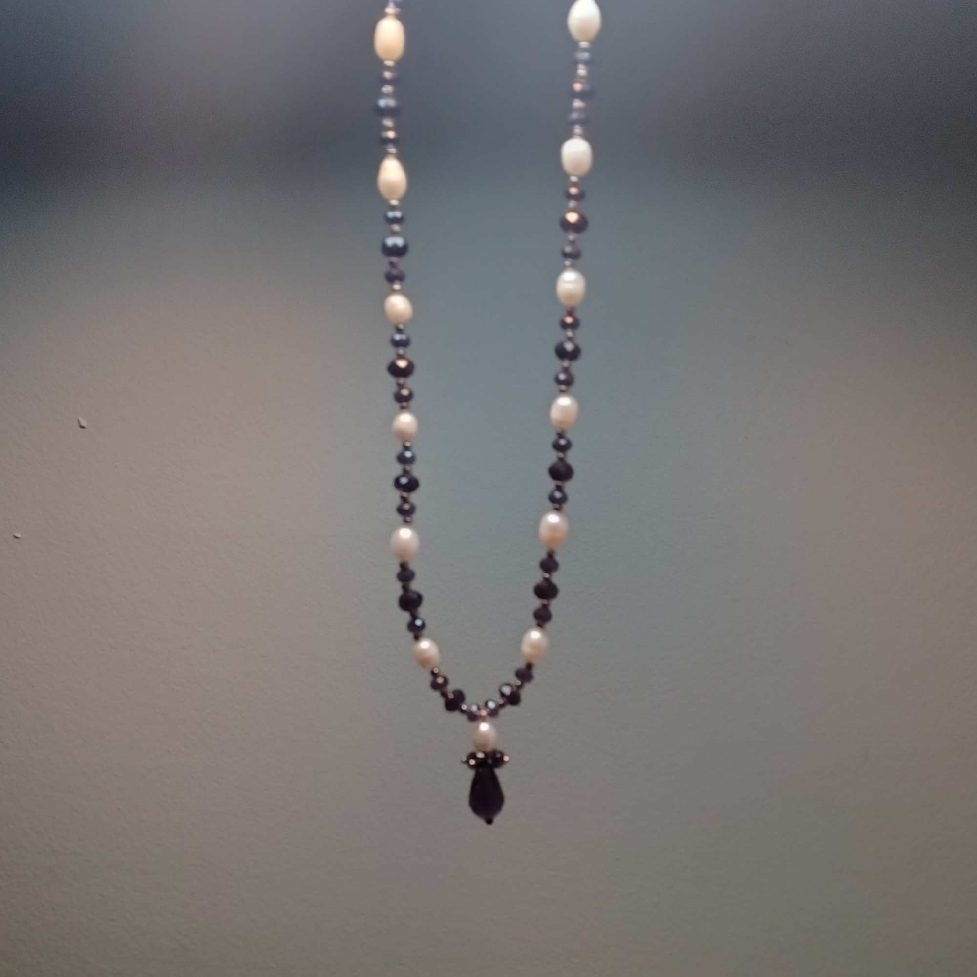 A beaded necklace with white and dark beads hangs against a plain wall.