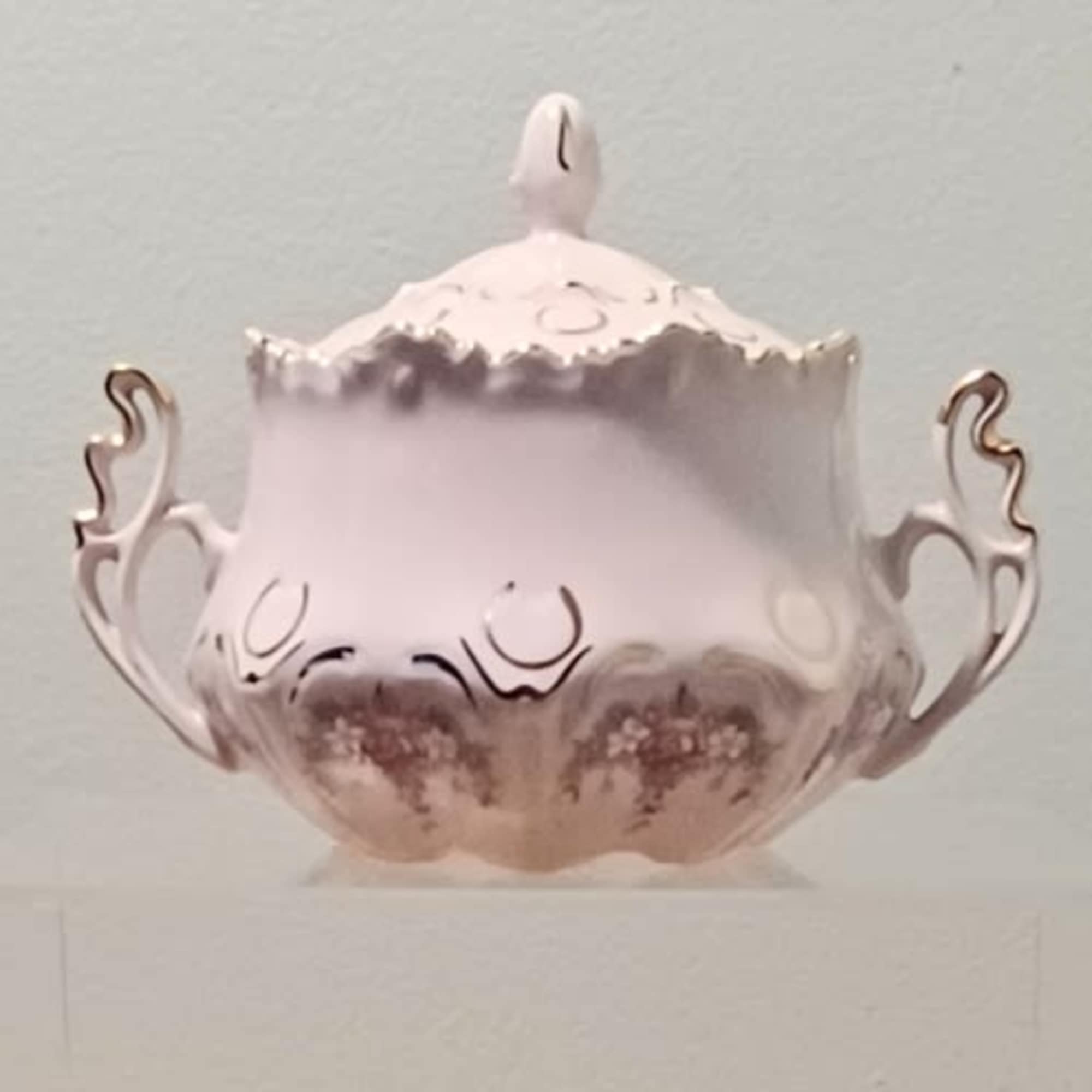 A pale pink decorative lidded bowl with ornate handles