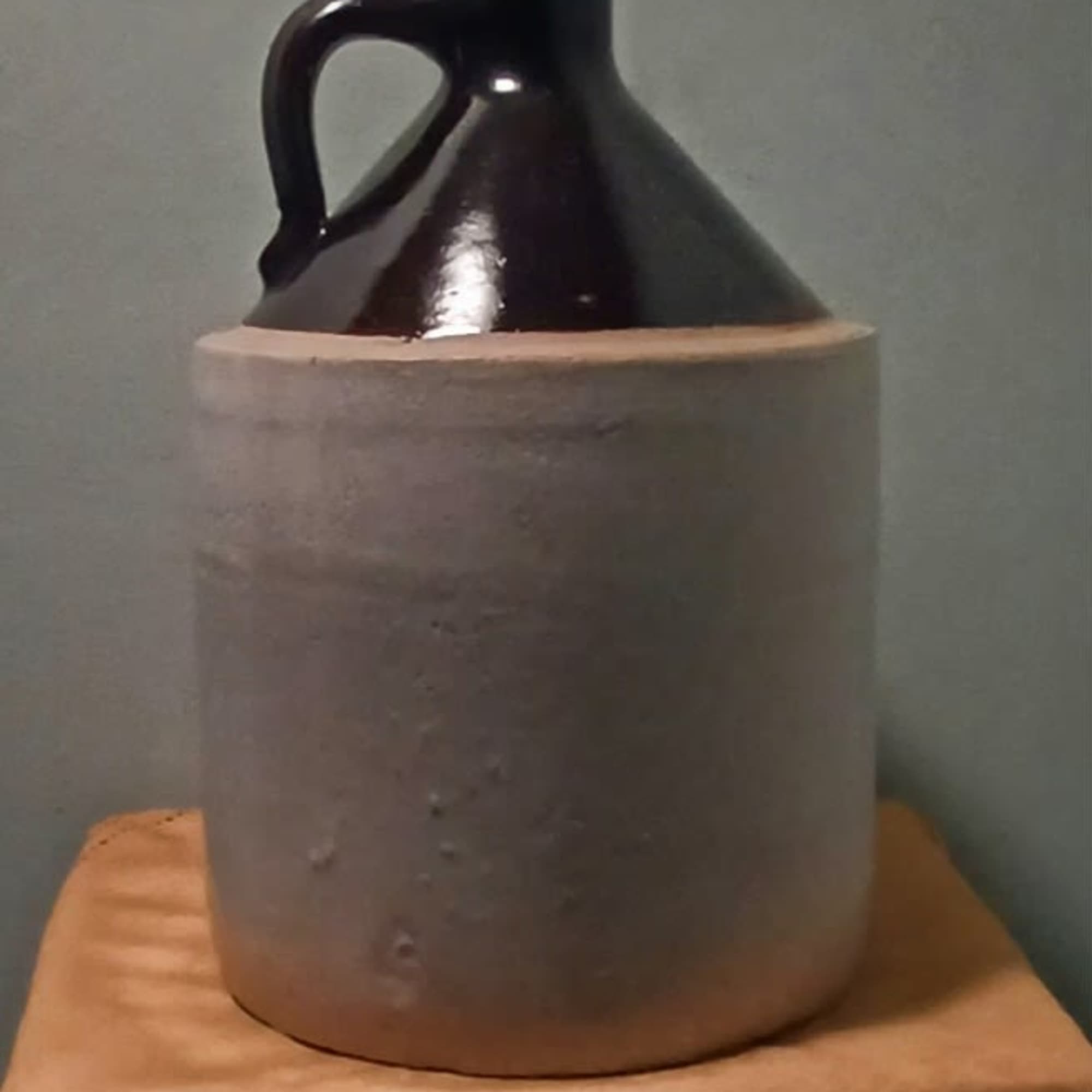 Dark ceramic jug in a beige sleeve on a wooden surface