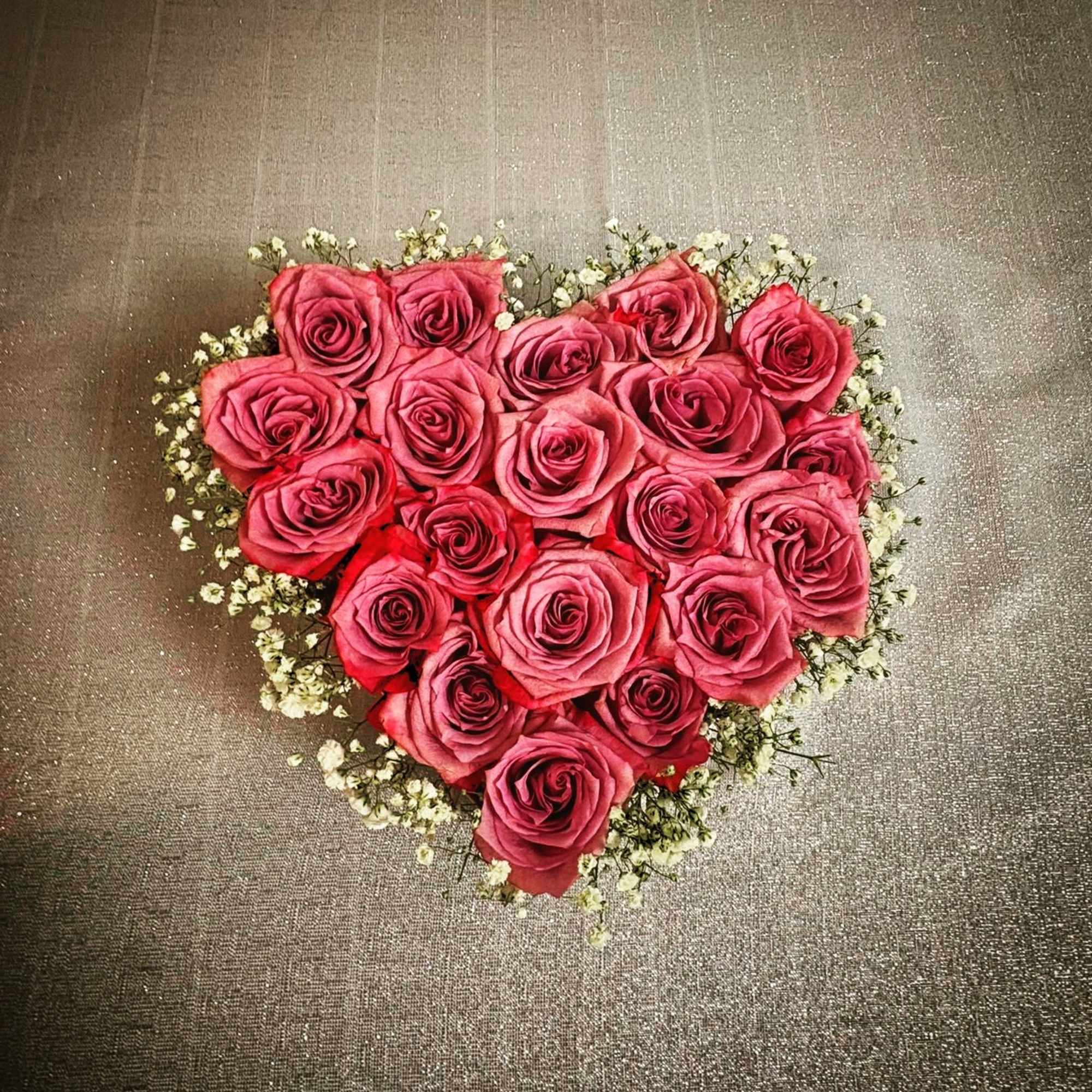 Heart-shaped bouquet of pink roses with small white filler flowers