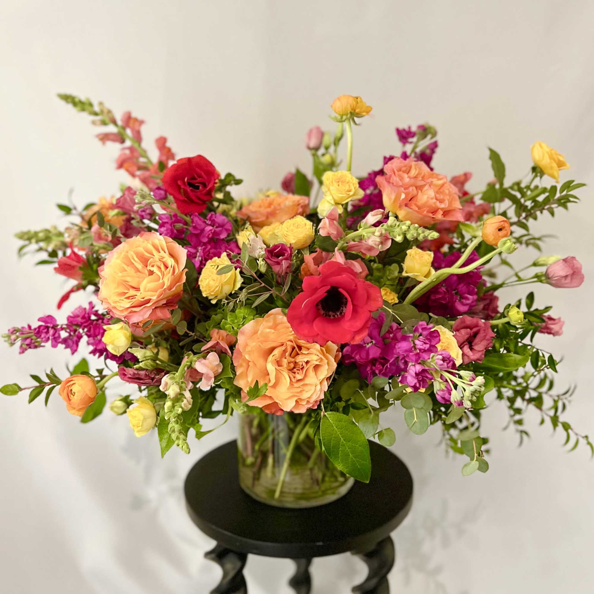 Mixed bouquet of peach, pink, yellow, and red flowers in a glass vase