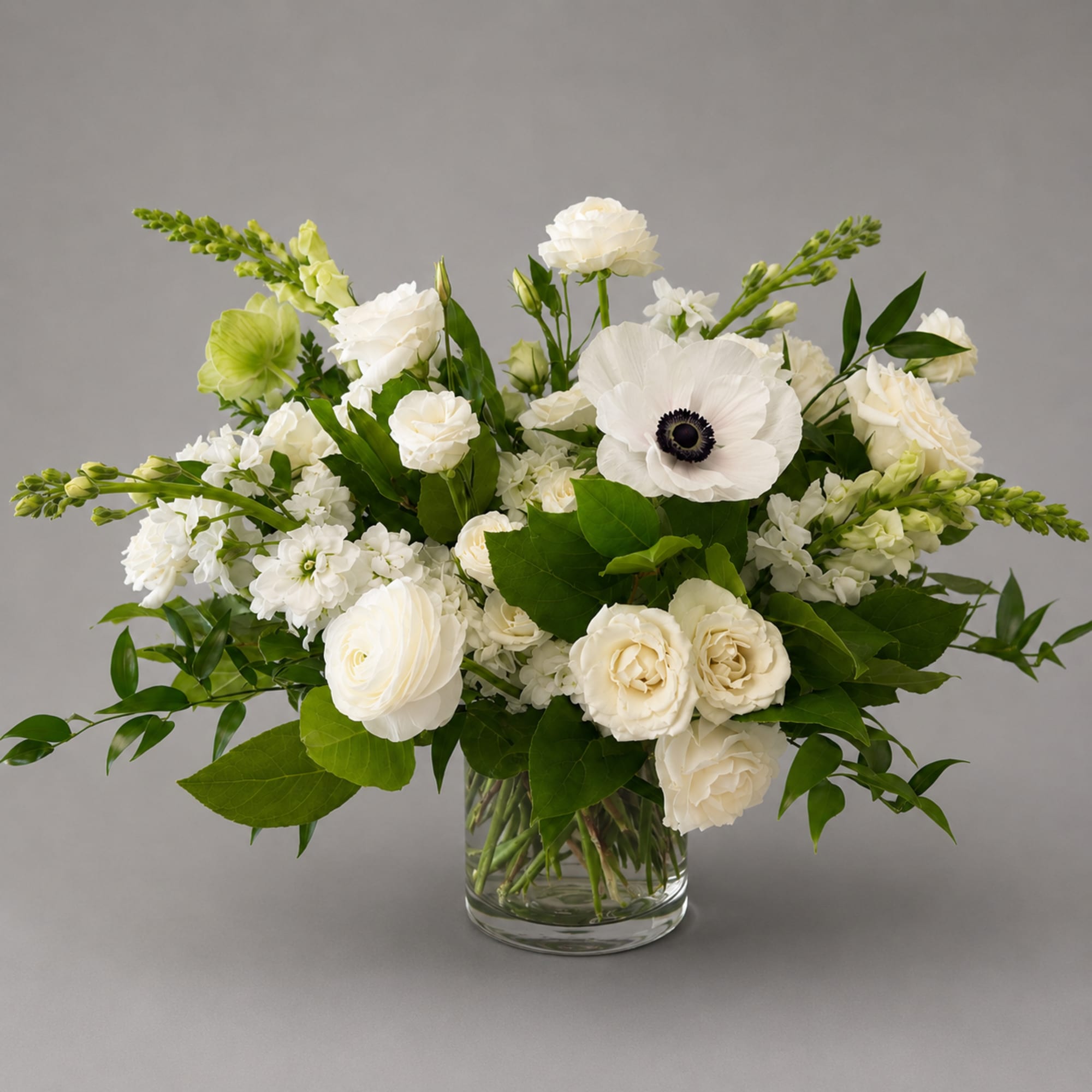 White floral arrangement in a clear glass vase with green accents