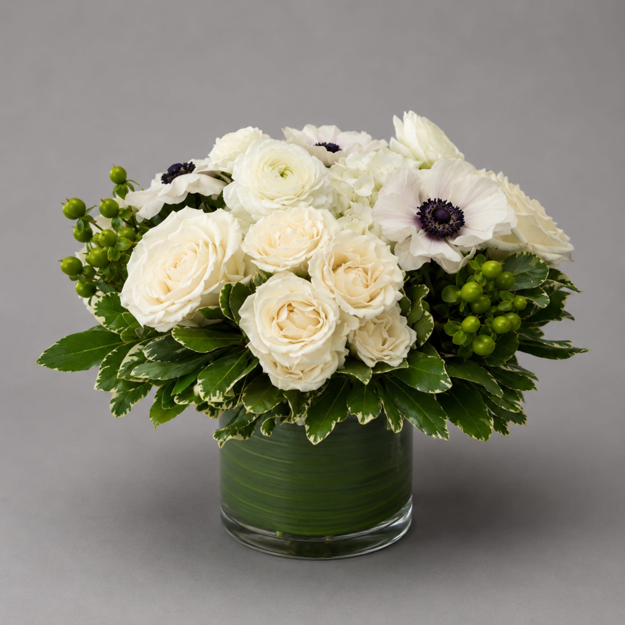 White roses and anemones arranged in a glass vase with green berries