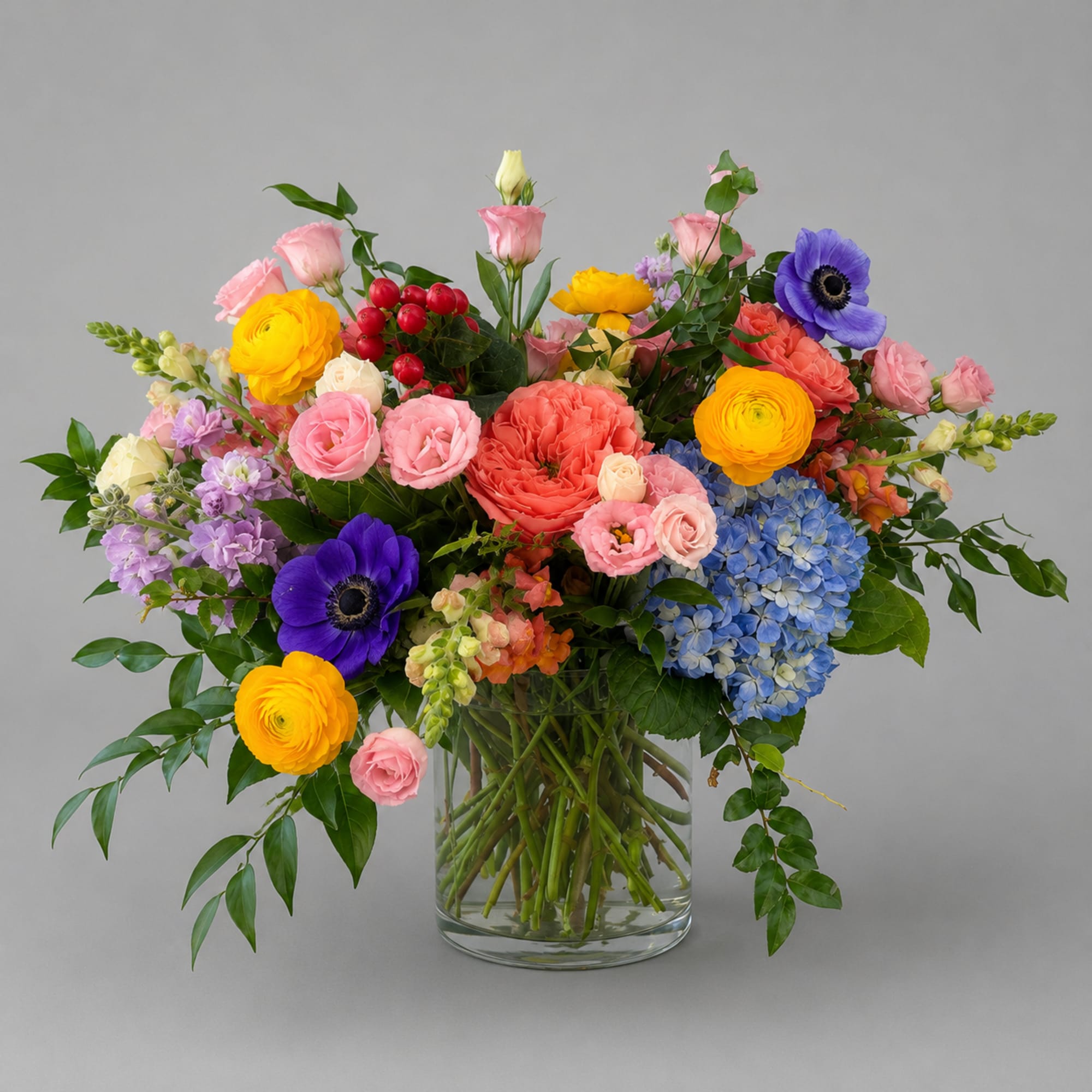 Colorful mixed bouquet in a clear glass vase with roses, ranunculus, anemones, and hydrangeas