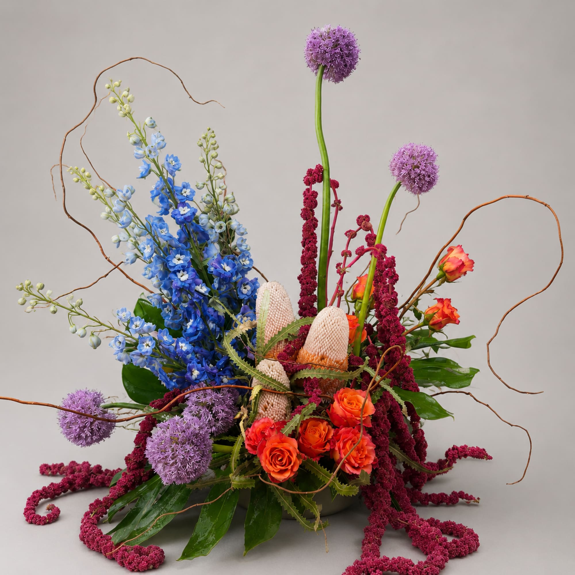 Tall floral arrangement with blue, purple, and orange blooms in a low container
