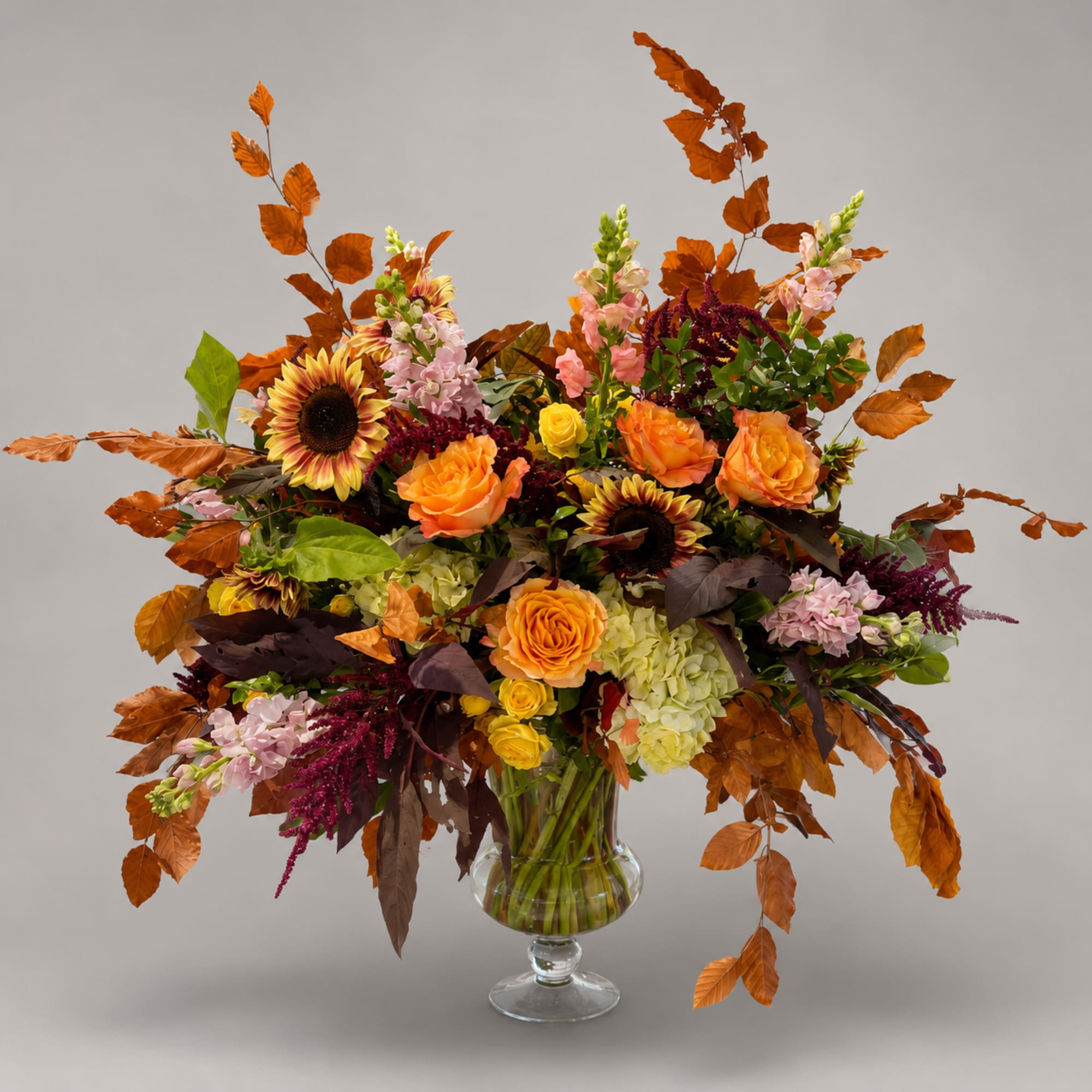 Large autumn bouquet in a clear glass vase with sunflowers, roses, and hydrangeas