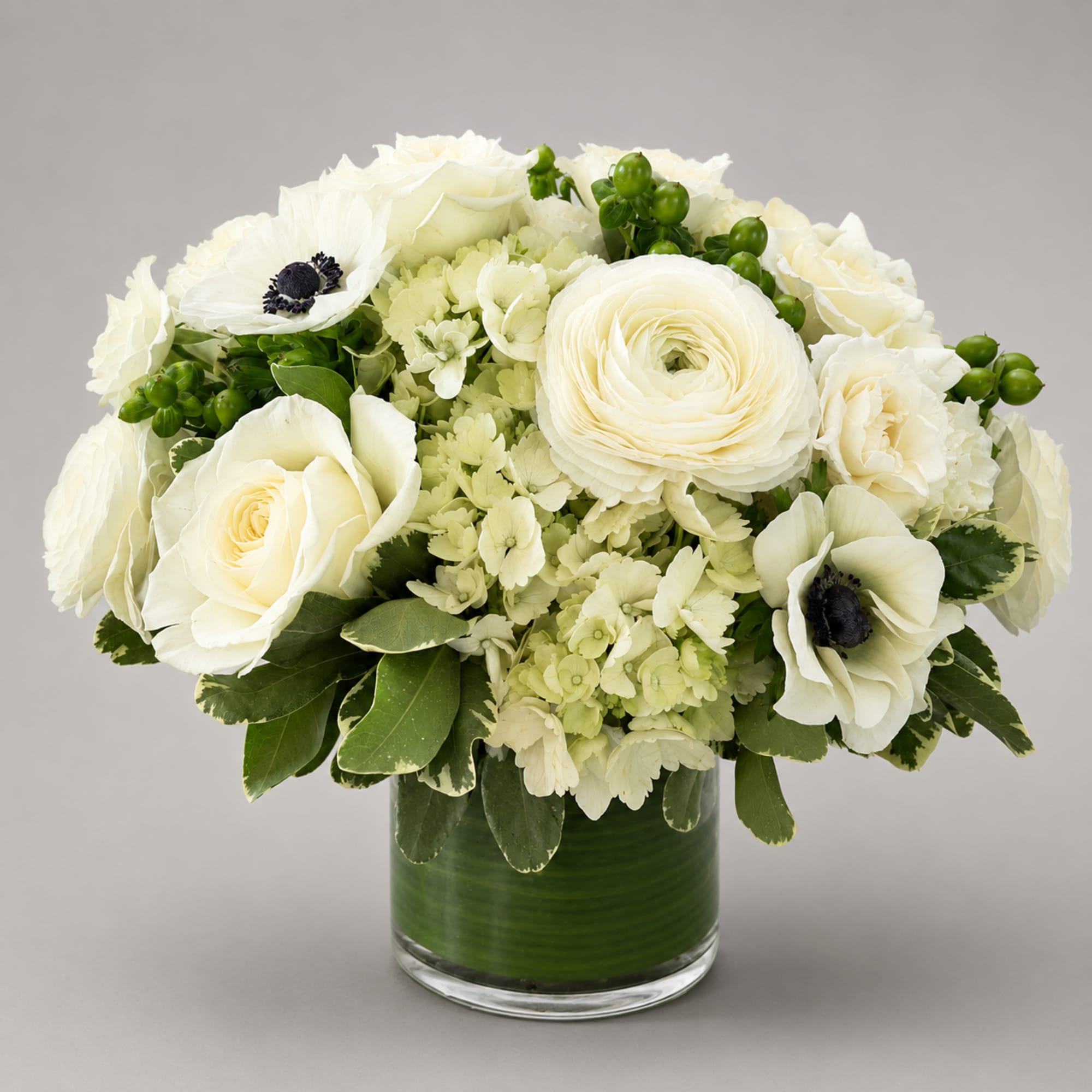 White floral arrangement in a glass vase with green berries