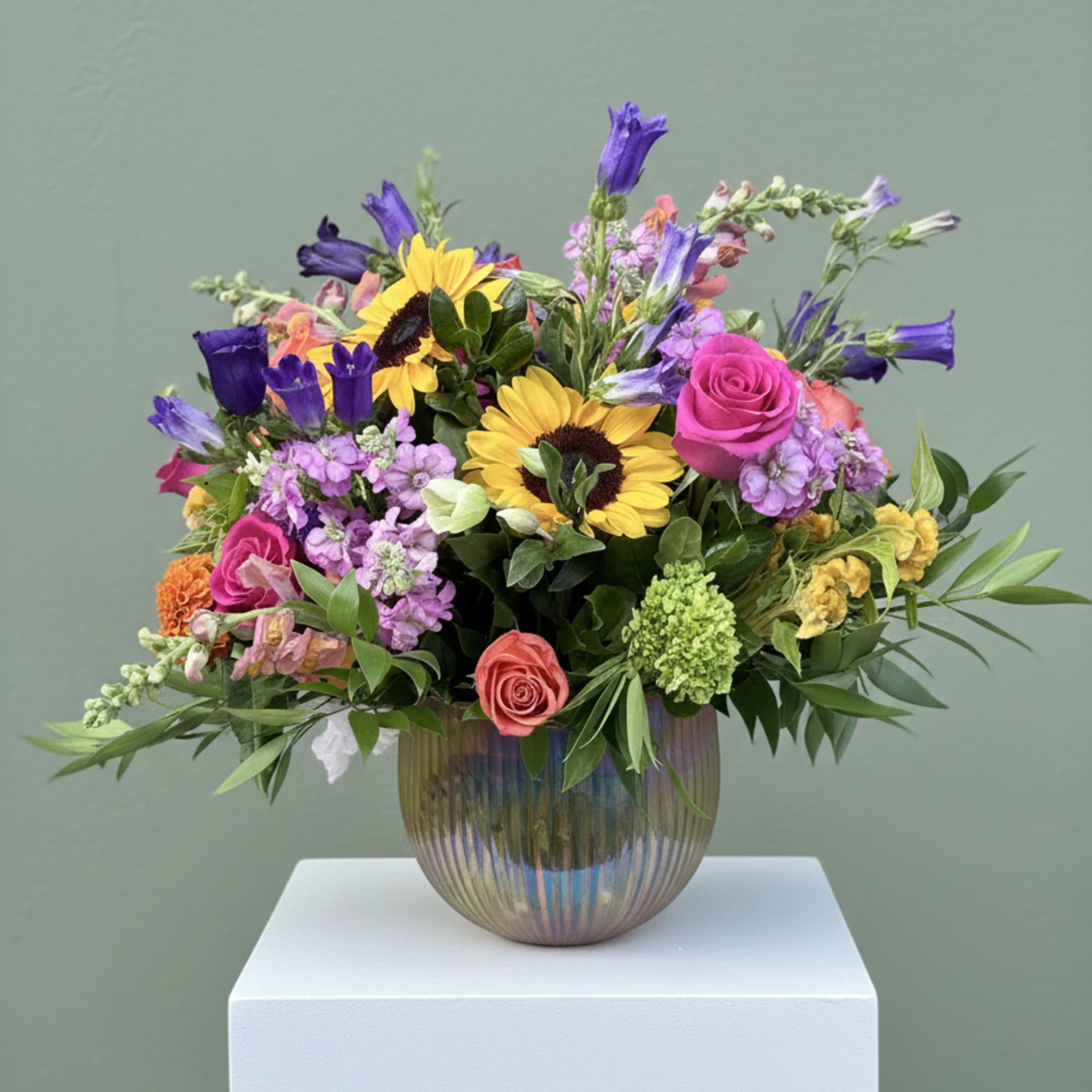 Mixed bouquet with sunflowers, roses, and purple blooms in a glass vase