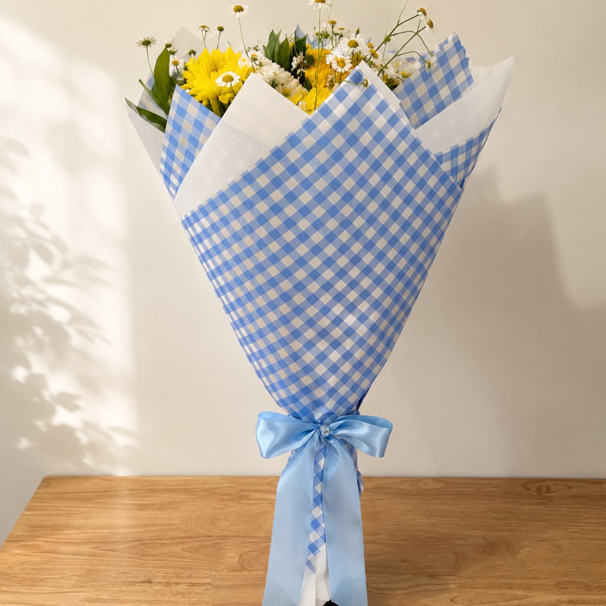 Bouquet of yellow daisies and white daisies wrapped in blue checkered paper