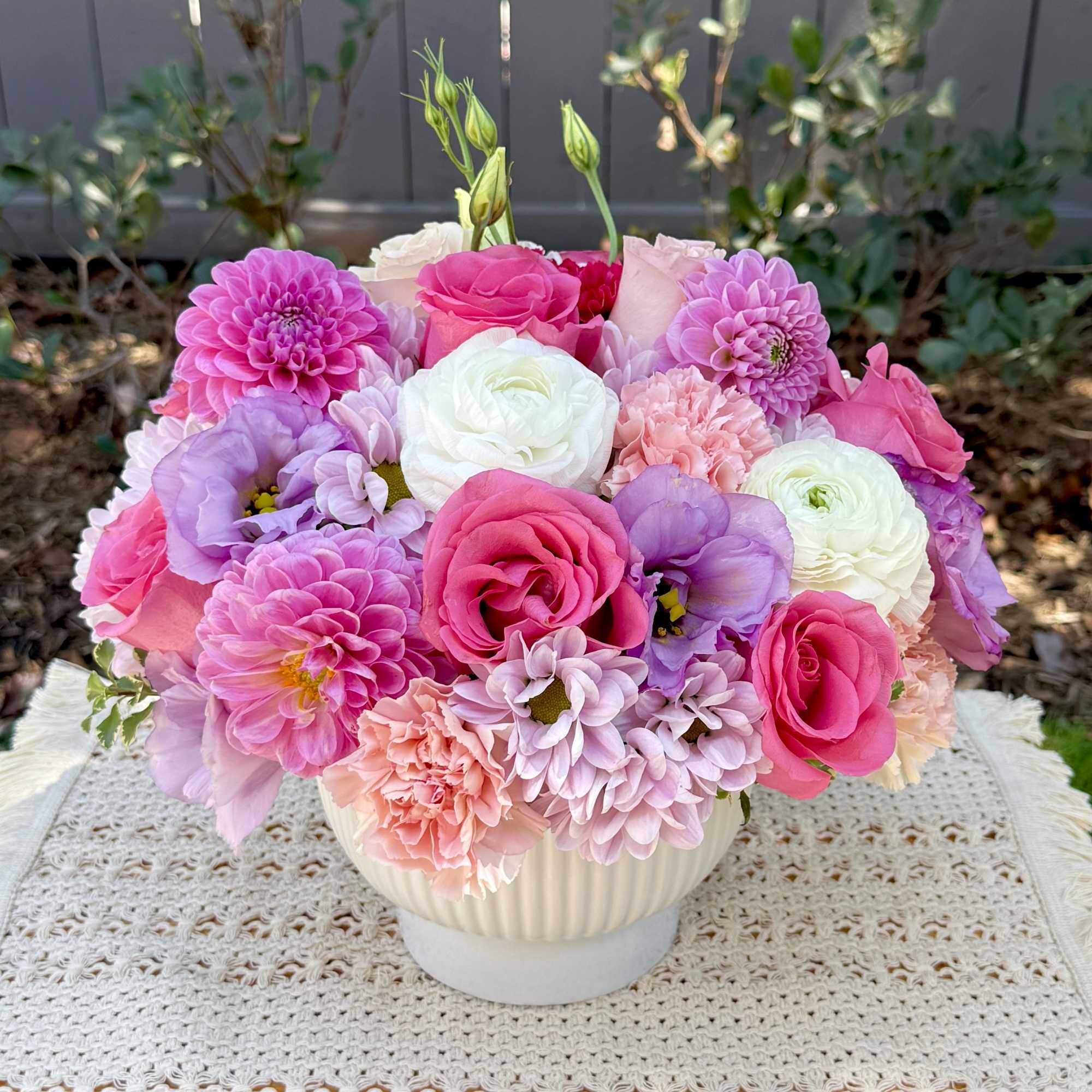 Pink, lavender, and white flowers arranged in a white bowl vase