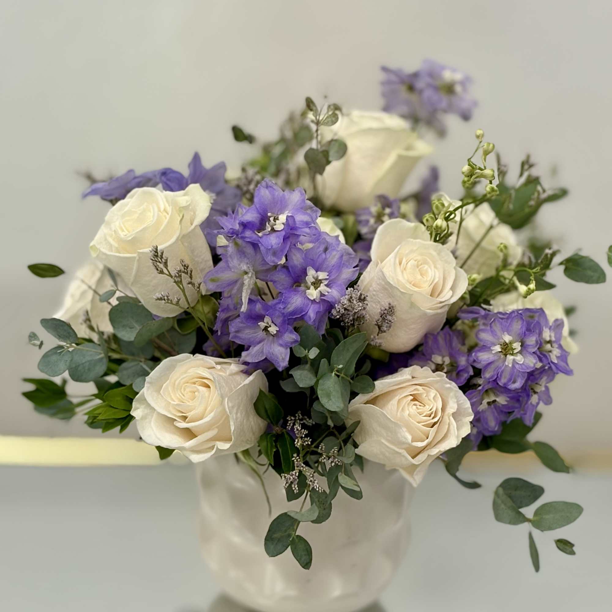 White roses and purple flowers arranged in a white vase