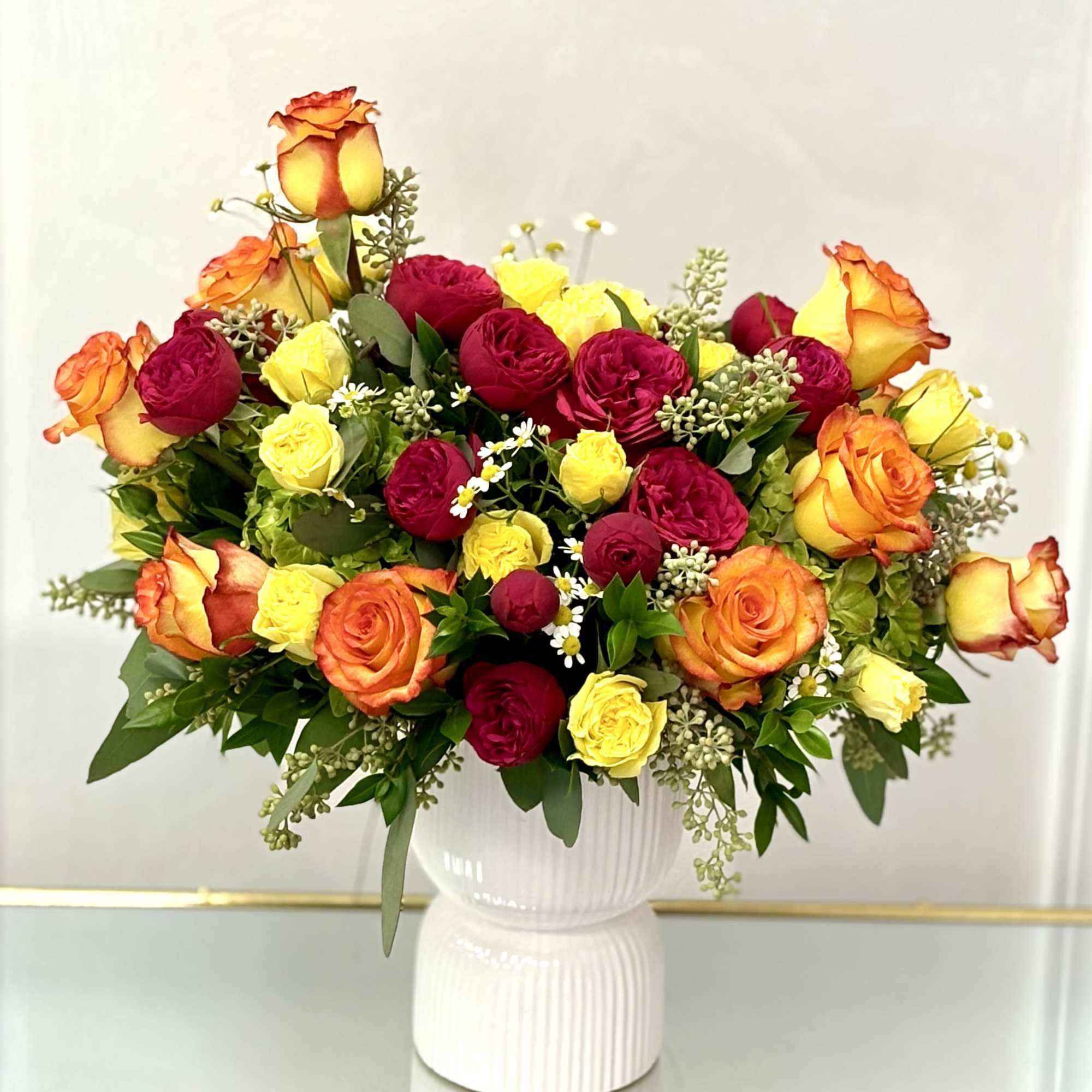 Bouquet of red, yellow, and orange roses in a white vase