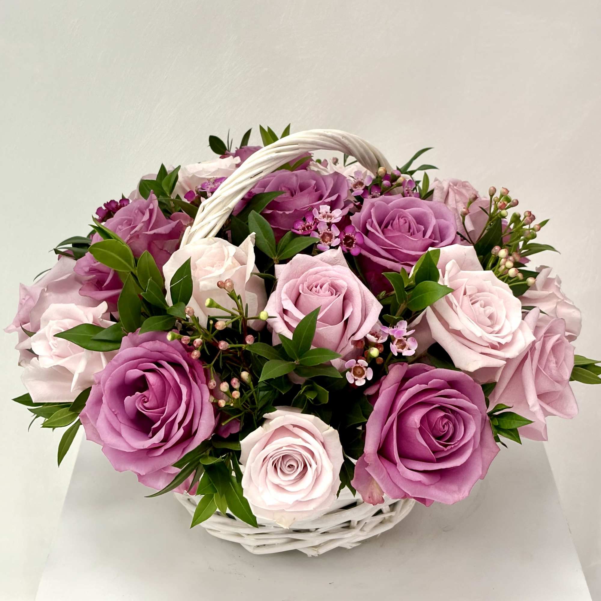 Basket of pink and lavender roses with small filler flowers