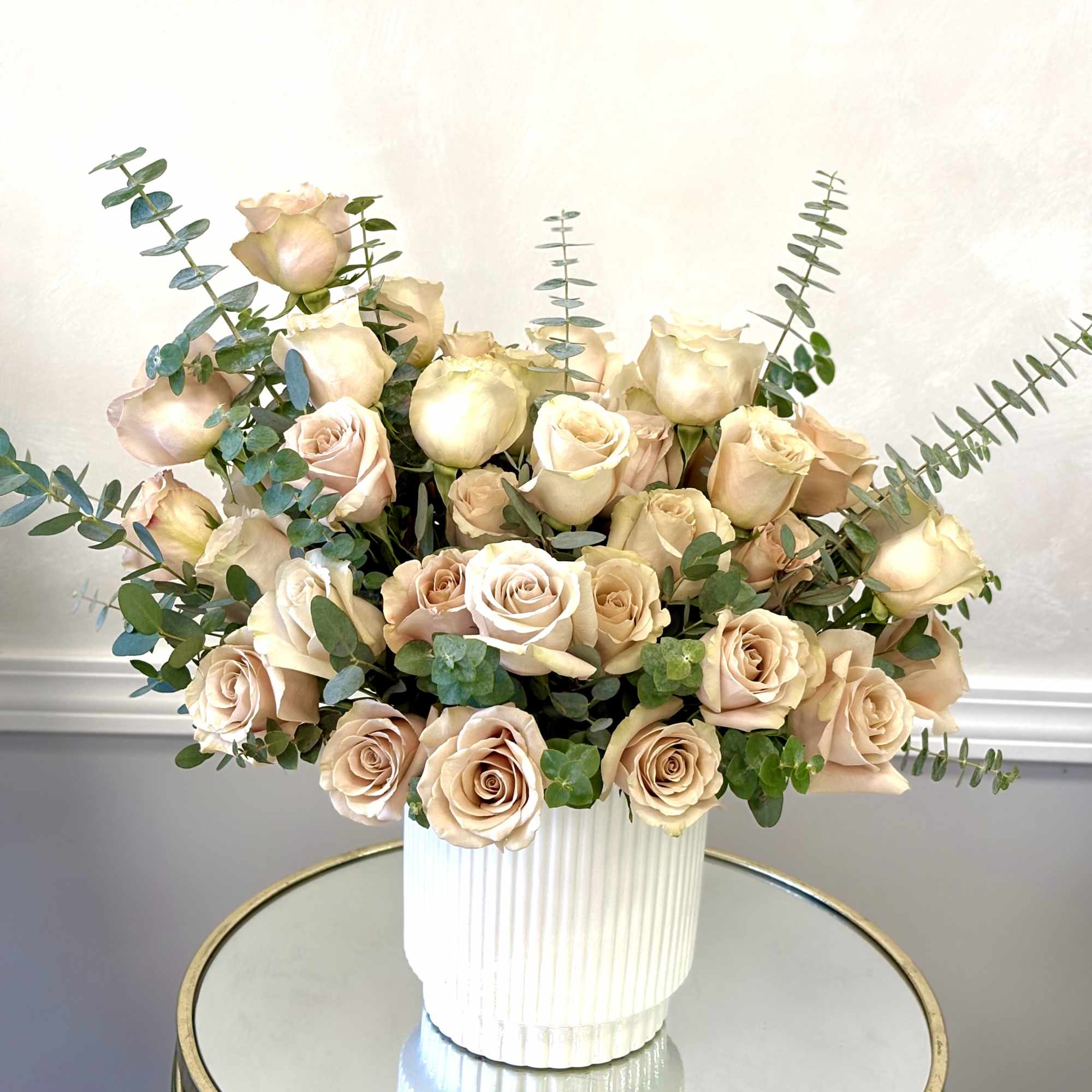 Peach roses arranged in a white ribbed vase with eucalyptus