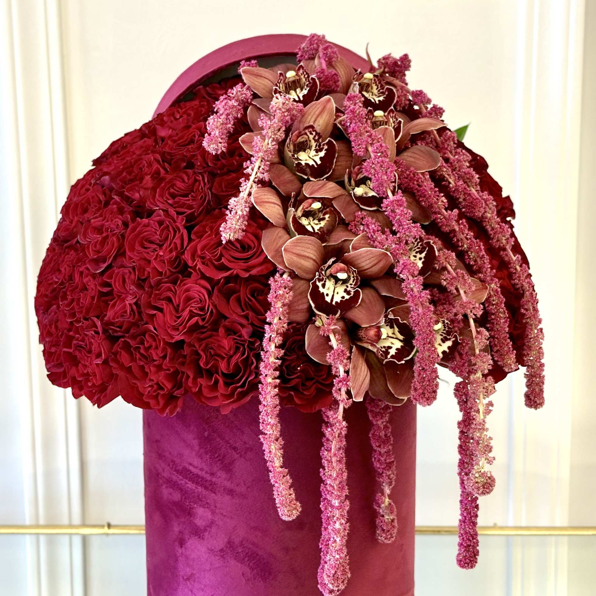 Large red floral arrangement with orchids and cascading pink blooms in a magenta cylinder