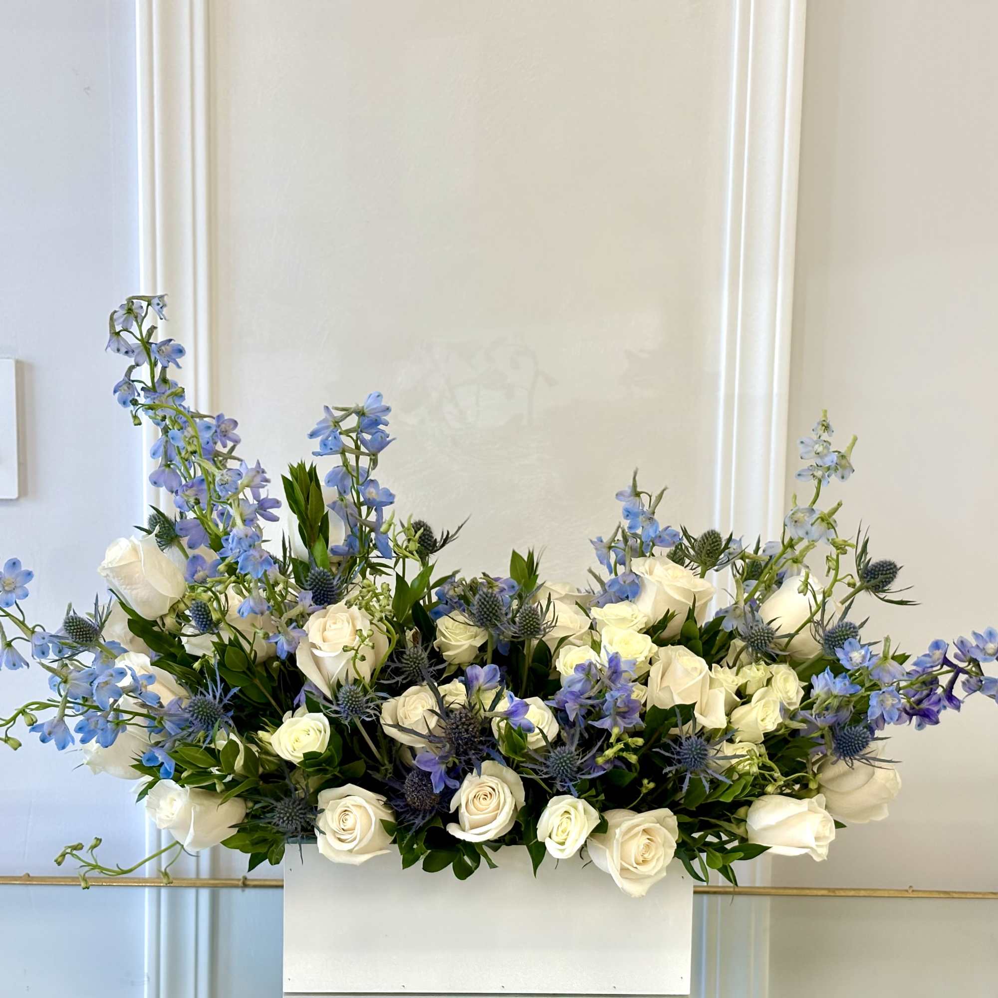 White roses and blue flowers arranged in a white rectangular container