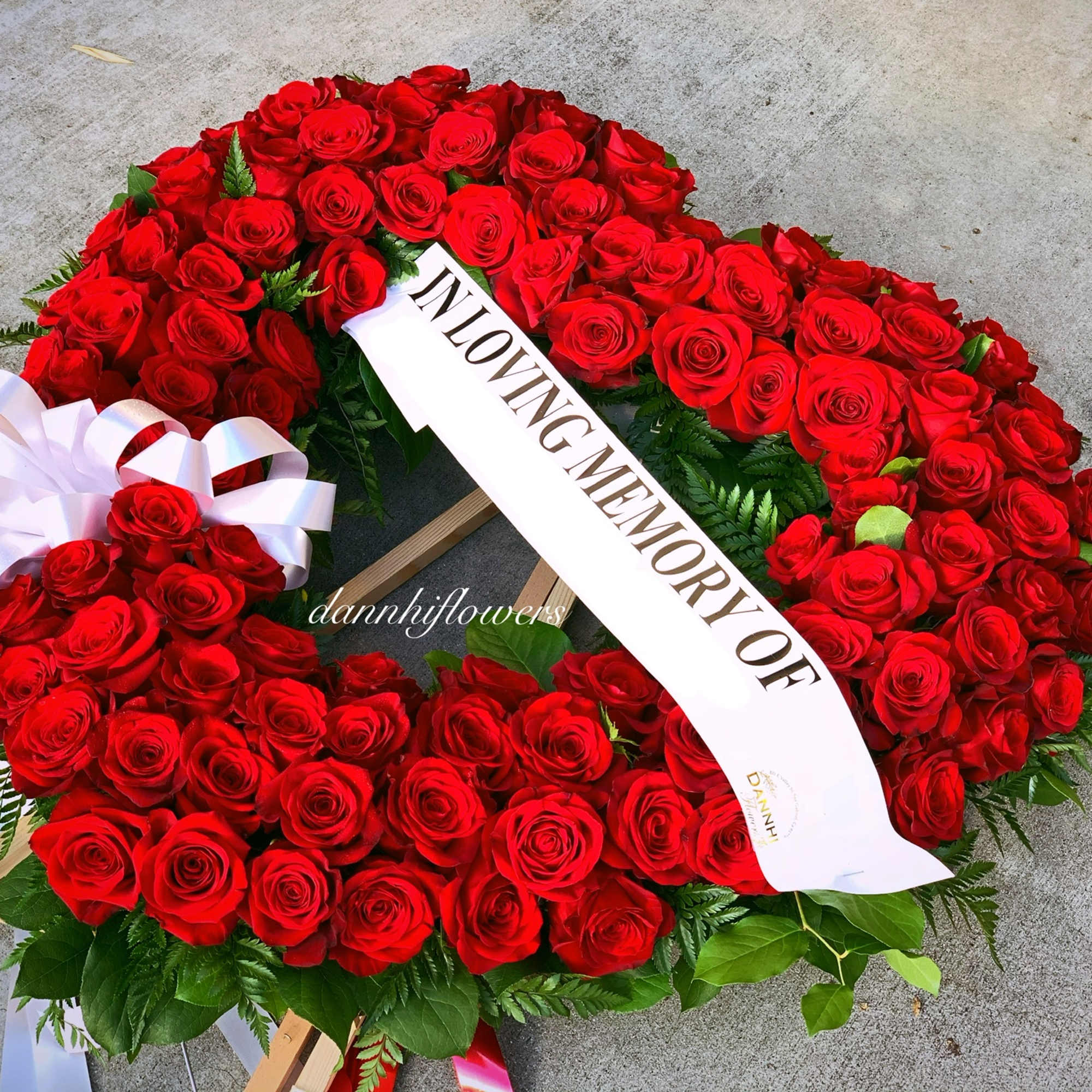 Heart-shaped wreath of red roses with a white memorial ribbon