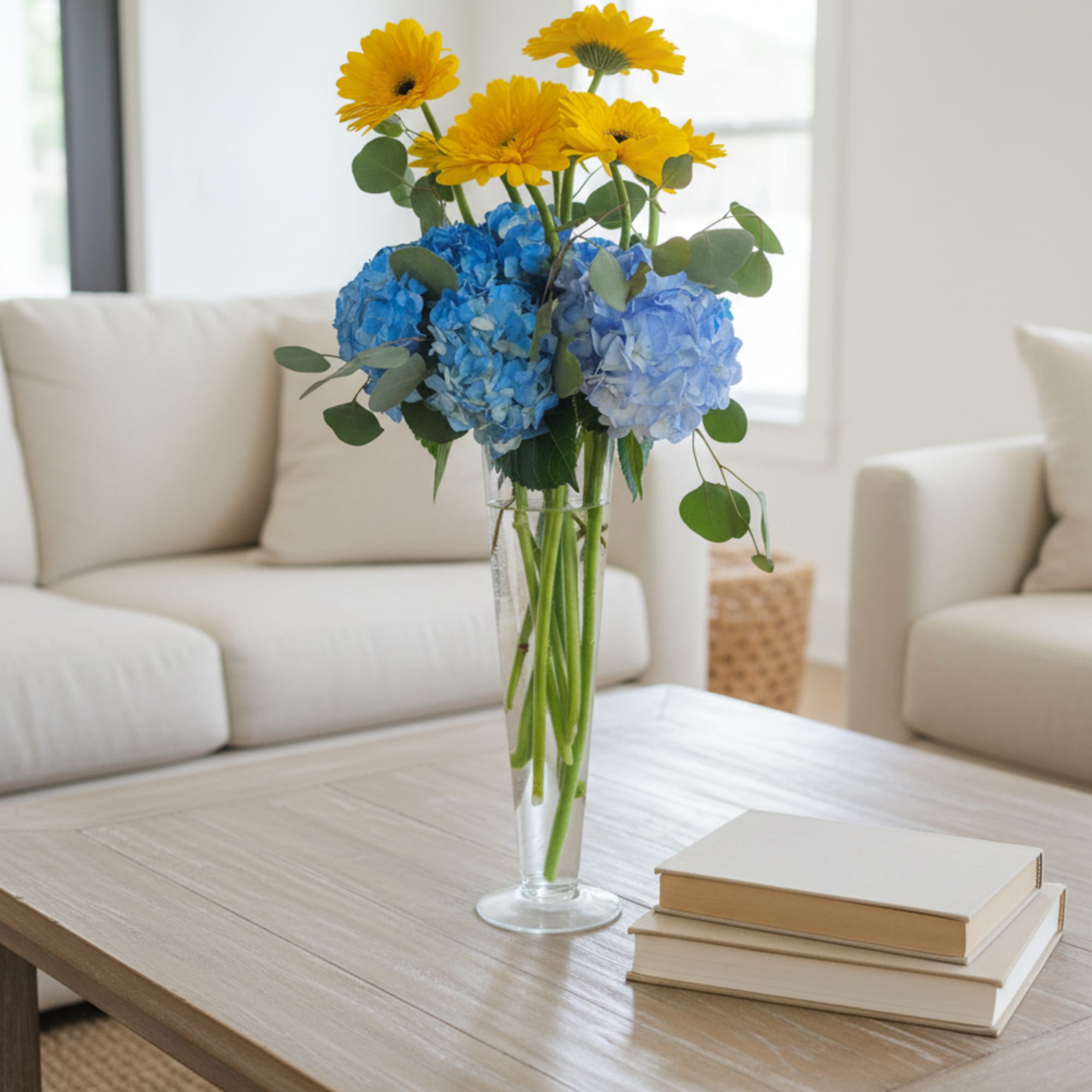 Yellow gerbera daisies and blue hydrangeas in a clear glass vase