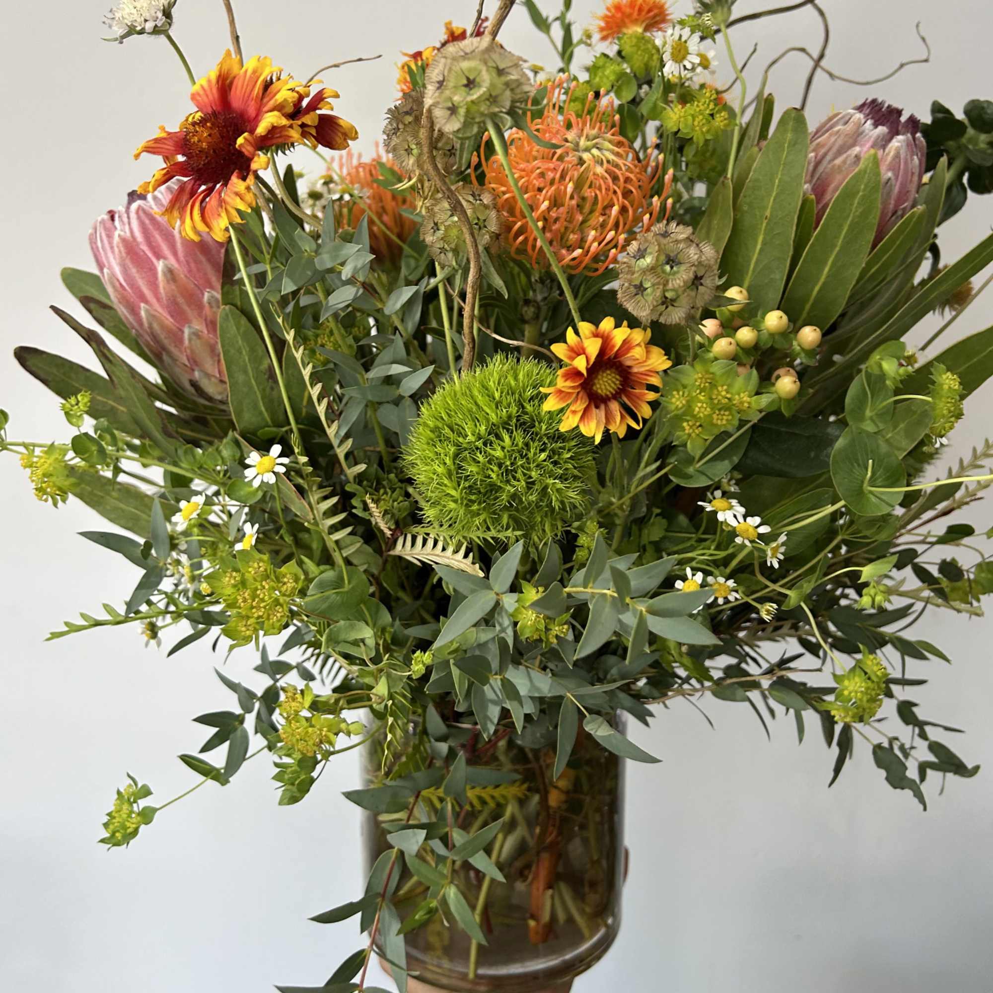 Seasonal native rustic flowers arranged into a vase with fillers and greens.