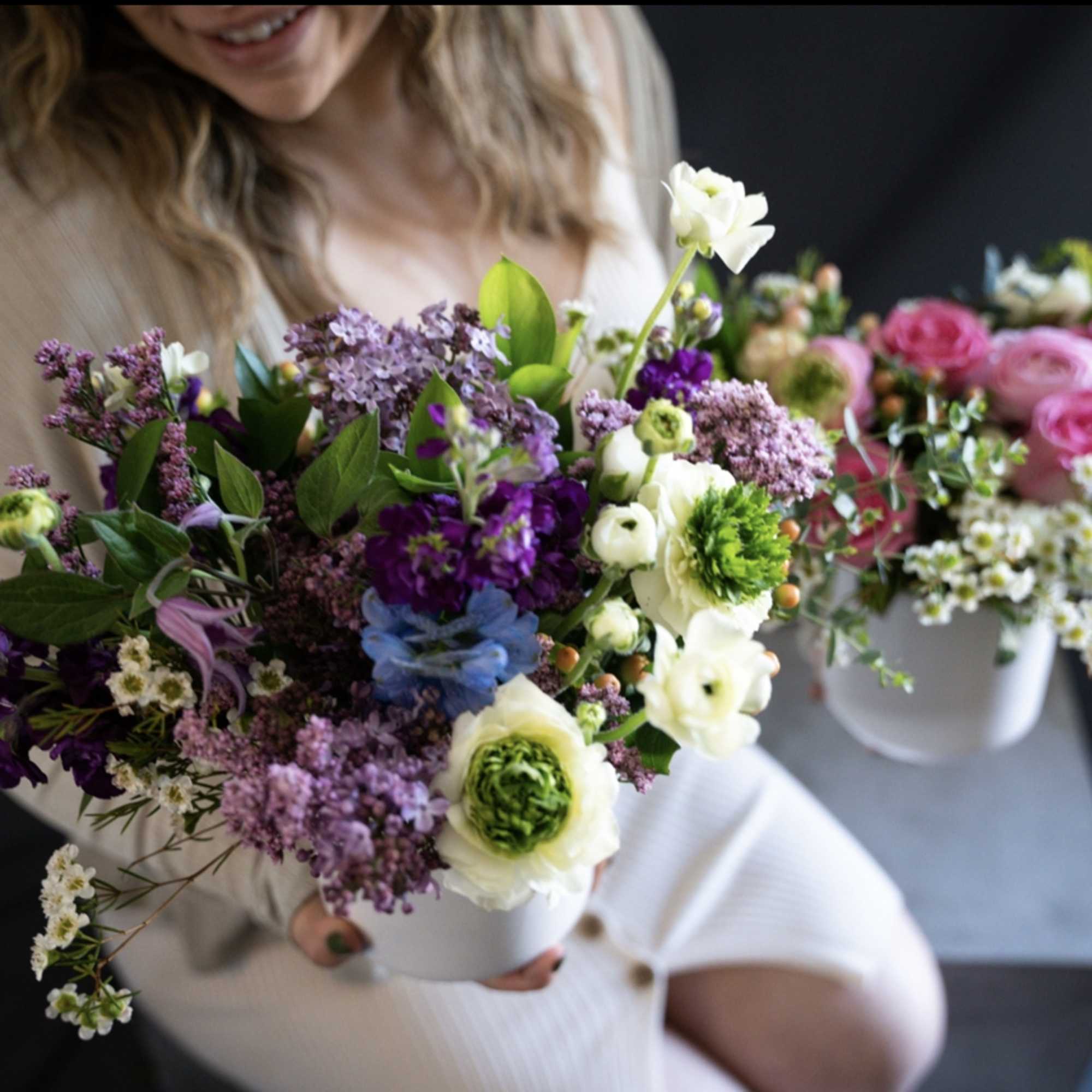 Woman holding a mixed bouquet in a white vase with pink and purple flowers