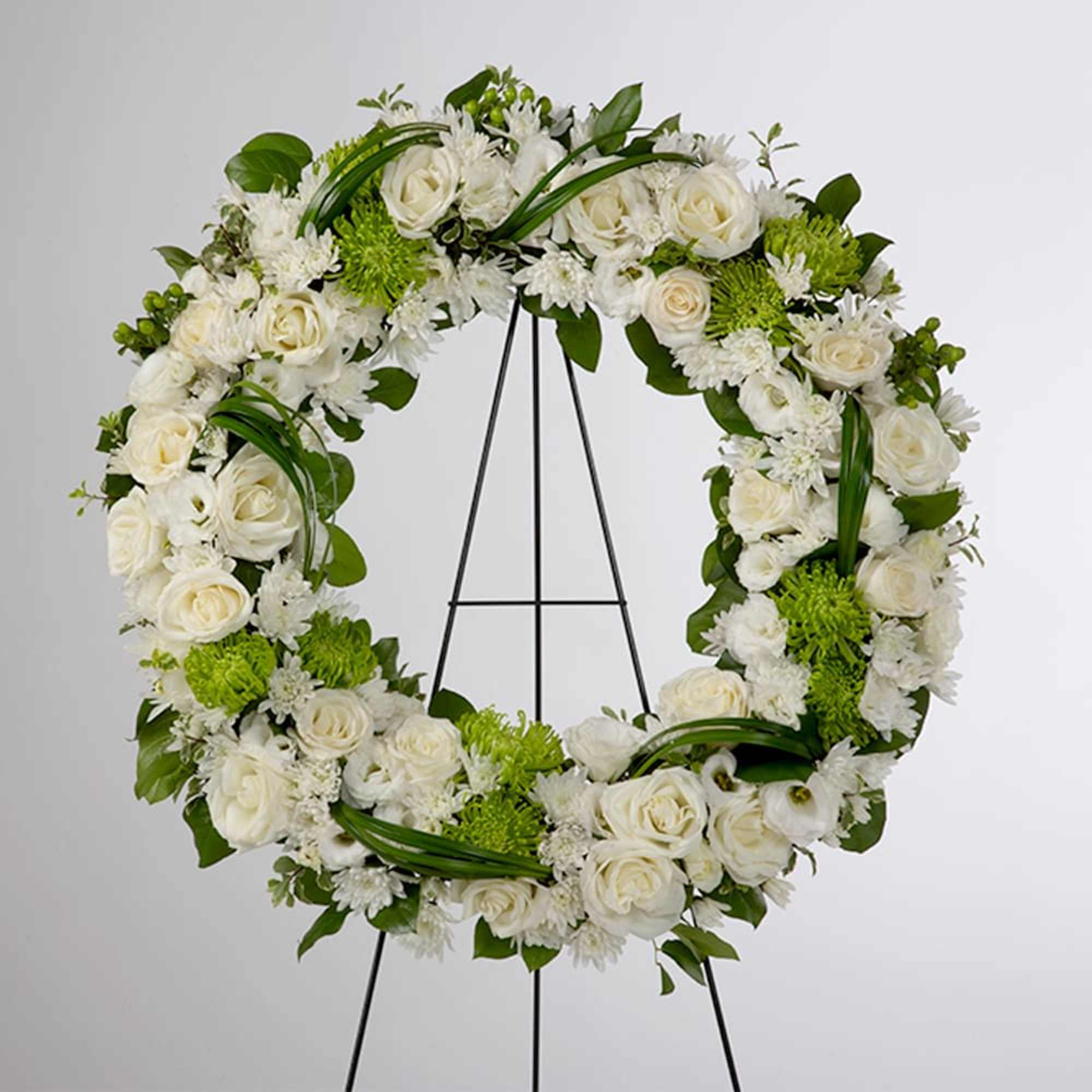 A full, circular sympathy wreath centered on creamy white roses creates an