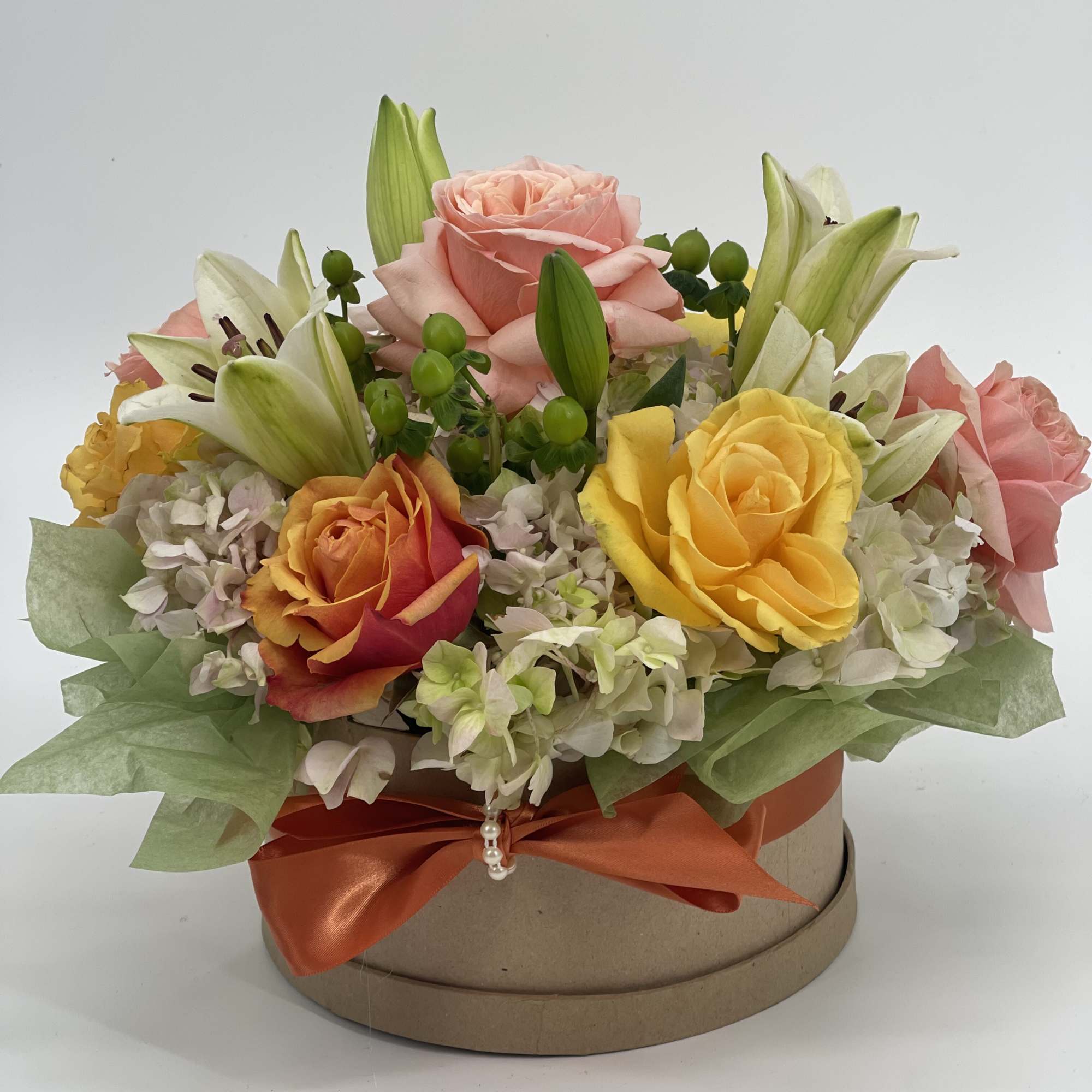 Mixed roses and lilies arranged in a round gift box with an orange ribbon