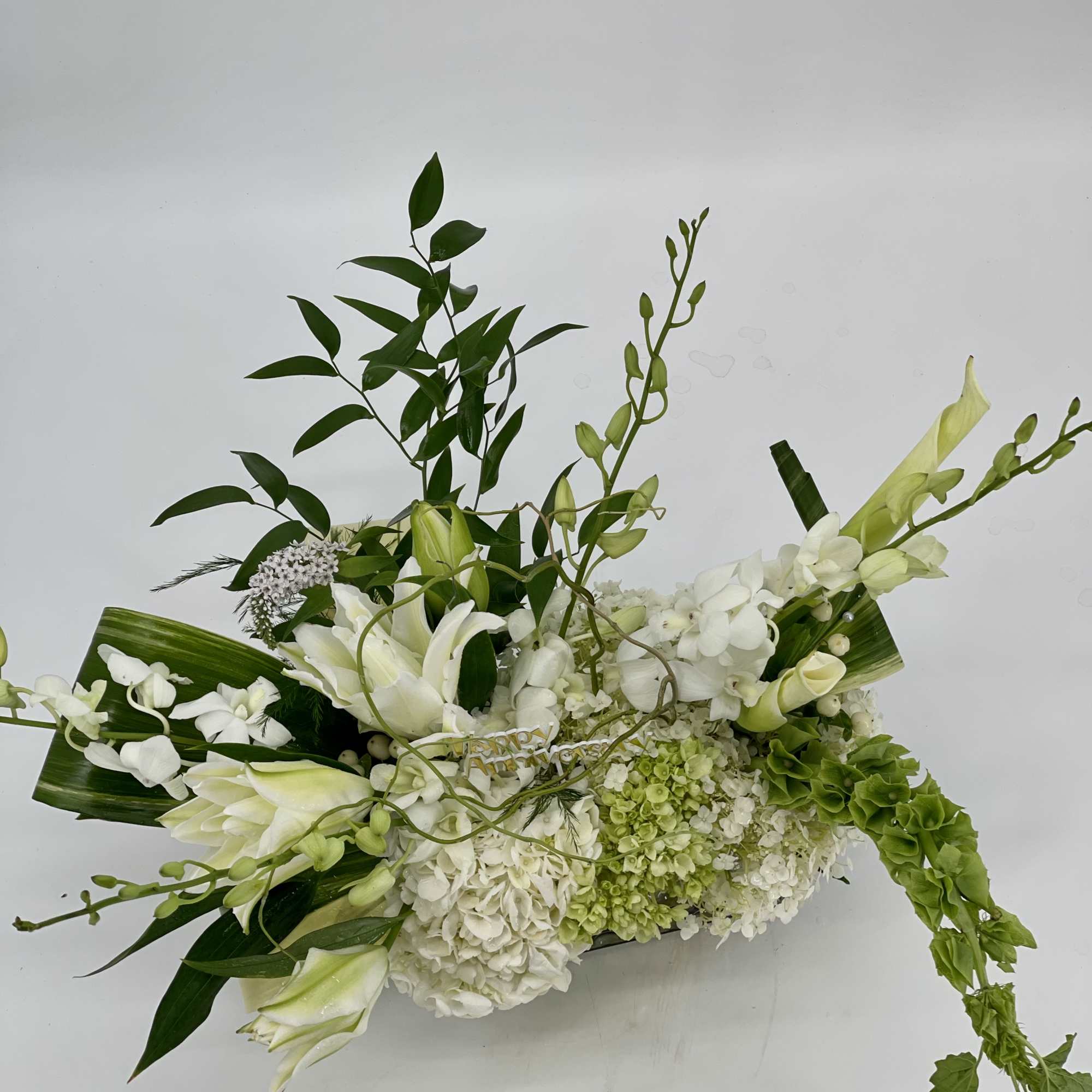 White floral arrangement with lilies, orchids, and hydrangeas in a low container