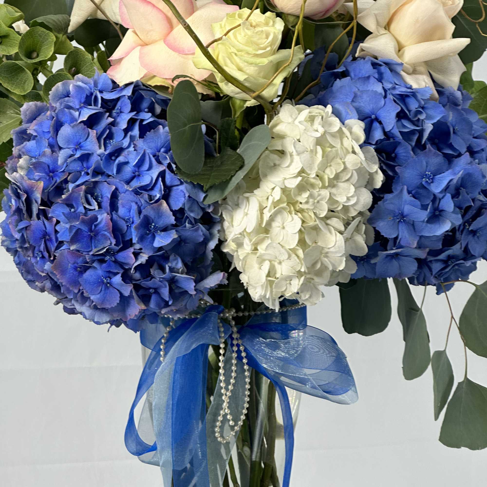 Blue and white hydrangeas with pink and white roses in a glass vase
