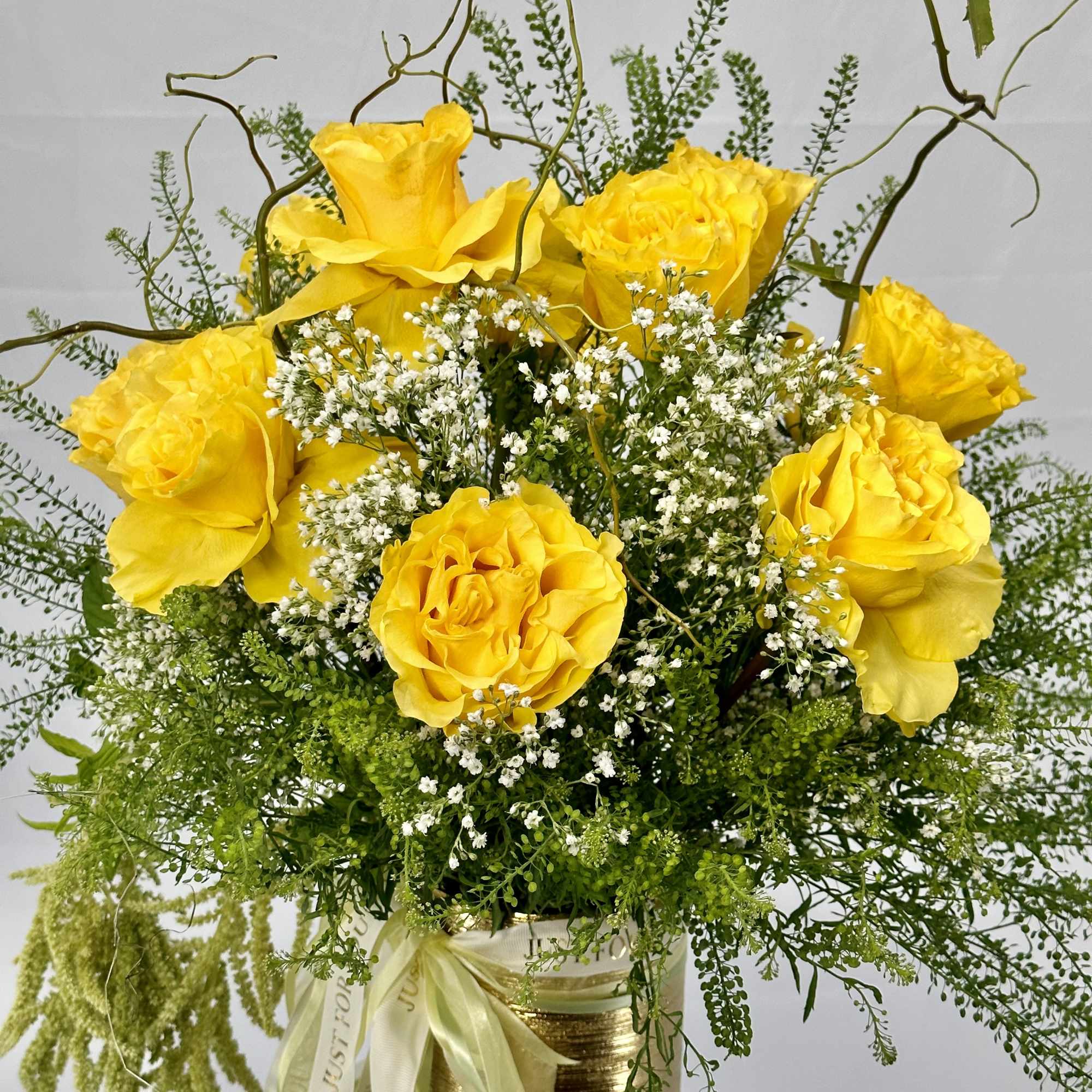 Yellow roses with white filler flowers in a gold vase