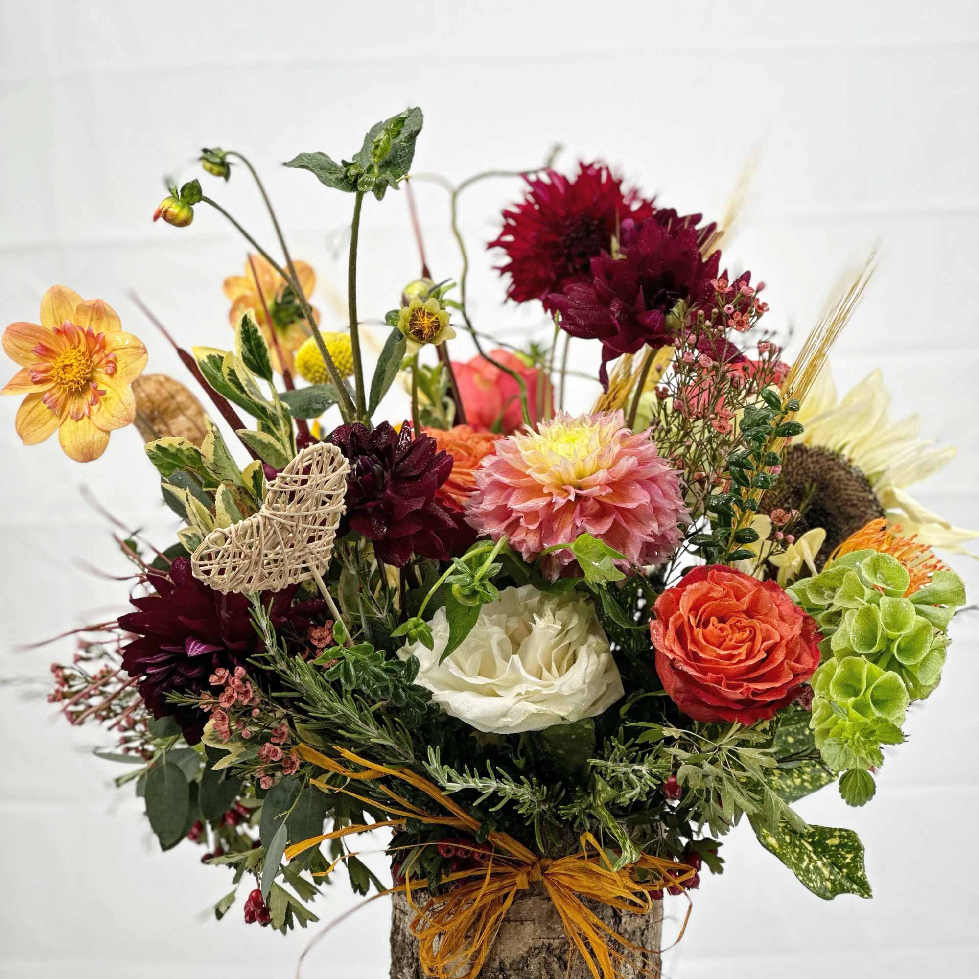 Mixed bouquet in a bark-covered container with burgundy, peach, white, and green flowers