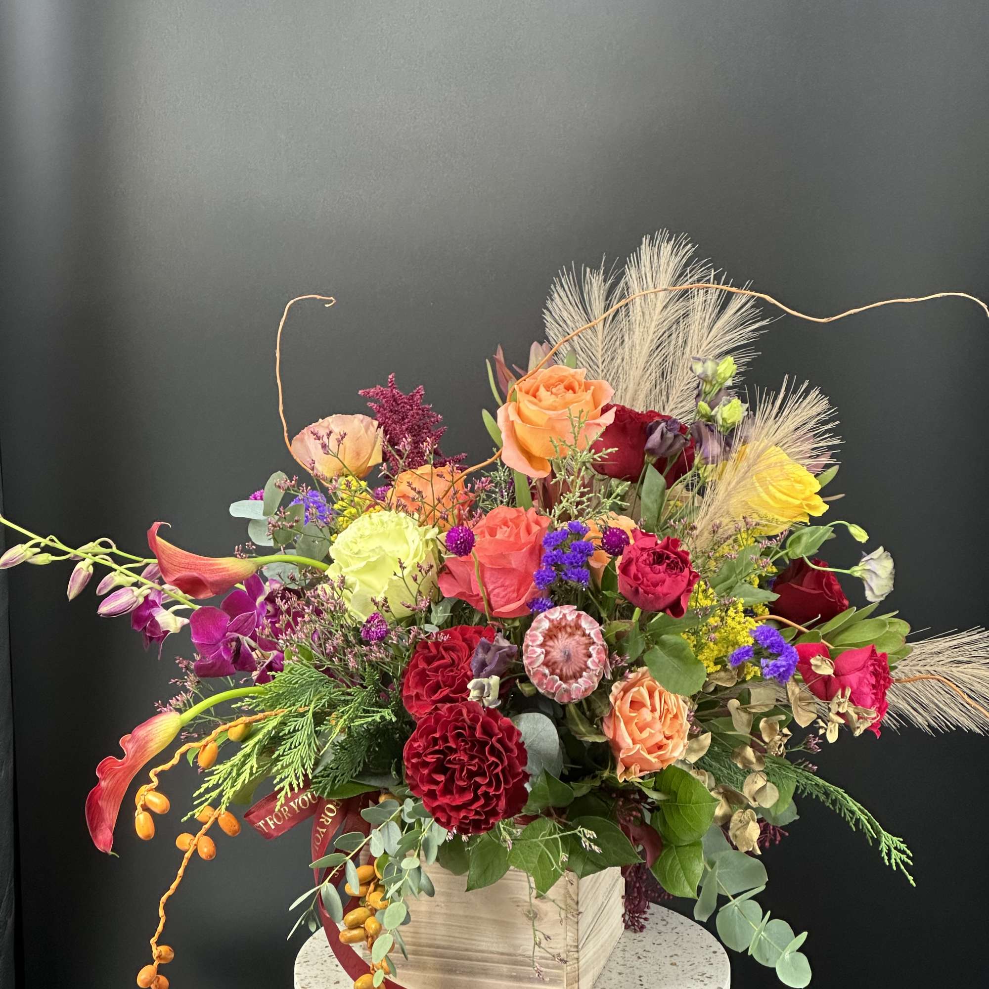 Colorful mixed flower arrangement in a wooden box with dried grasses