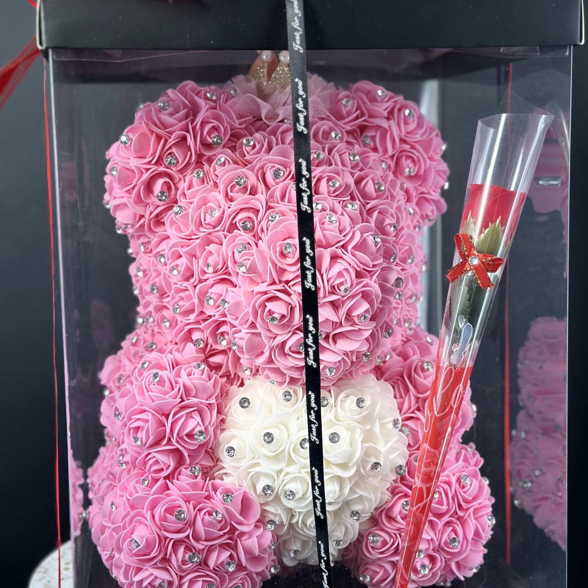 Pink rose teddy bear in a clear gift box with chocolates and a red ribbon