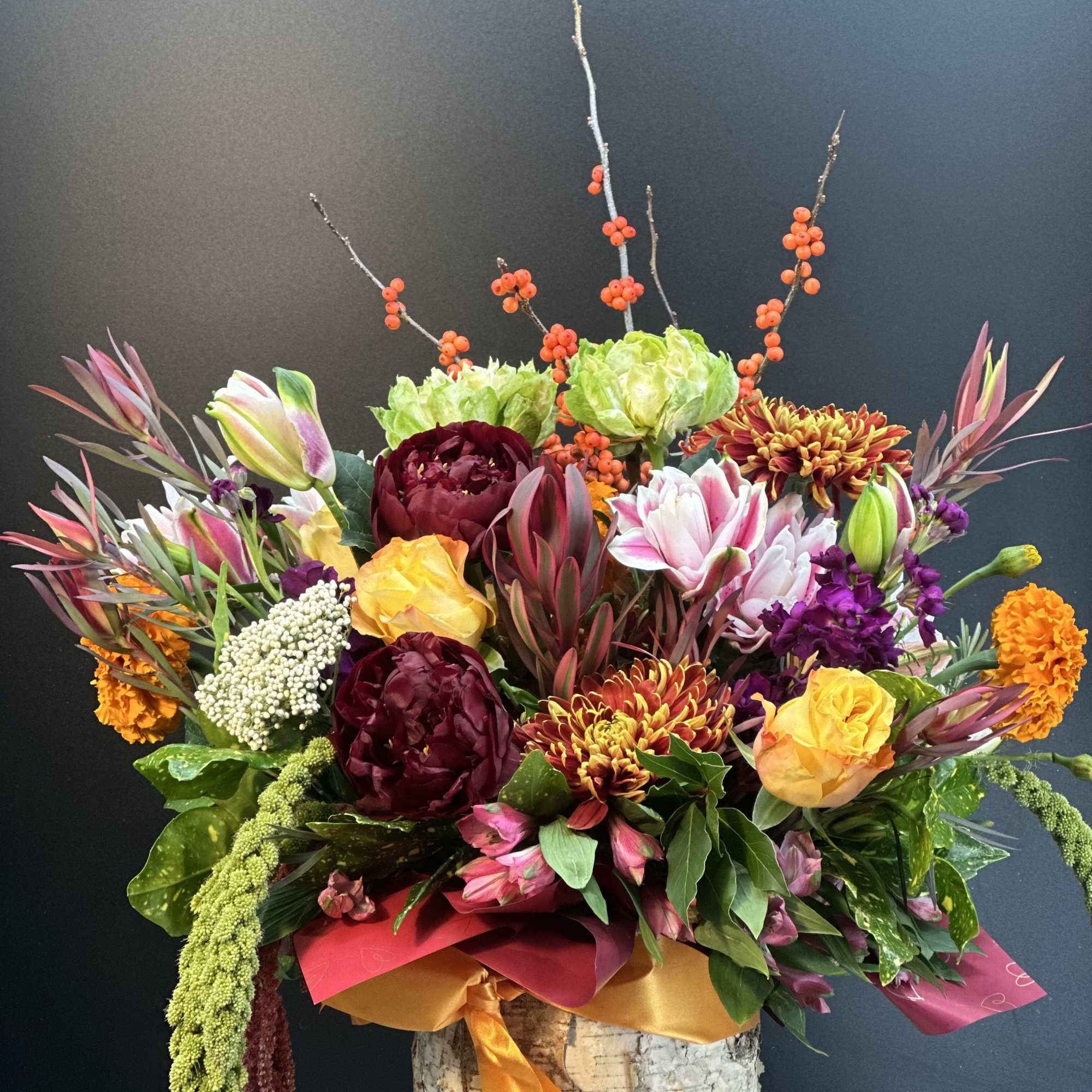 Colorful floral arrangement in a birch container with tall berry branches