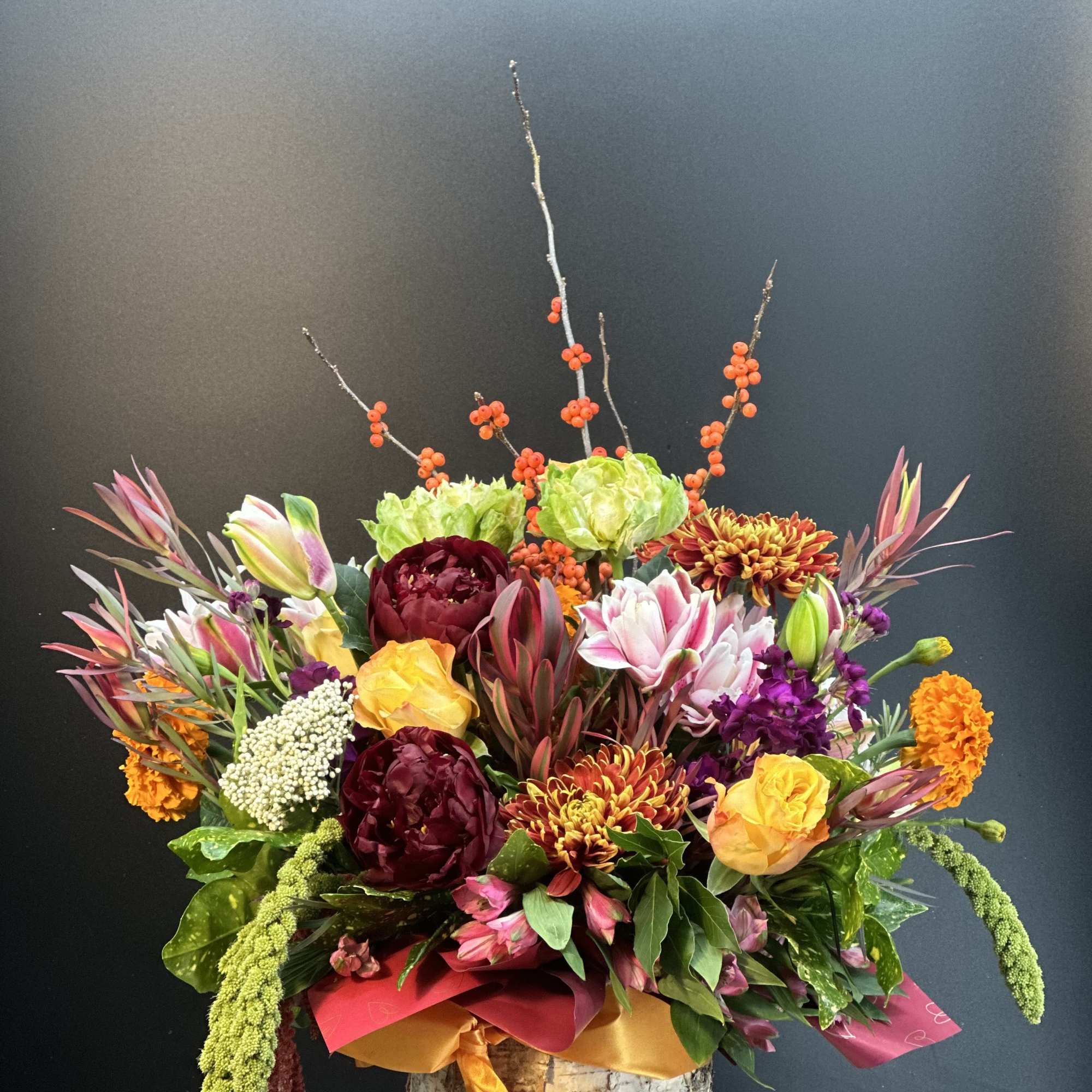 Colorful floral arrangement in a birch bark container with tall berry branches