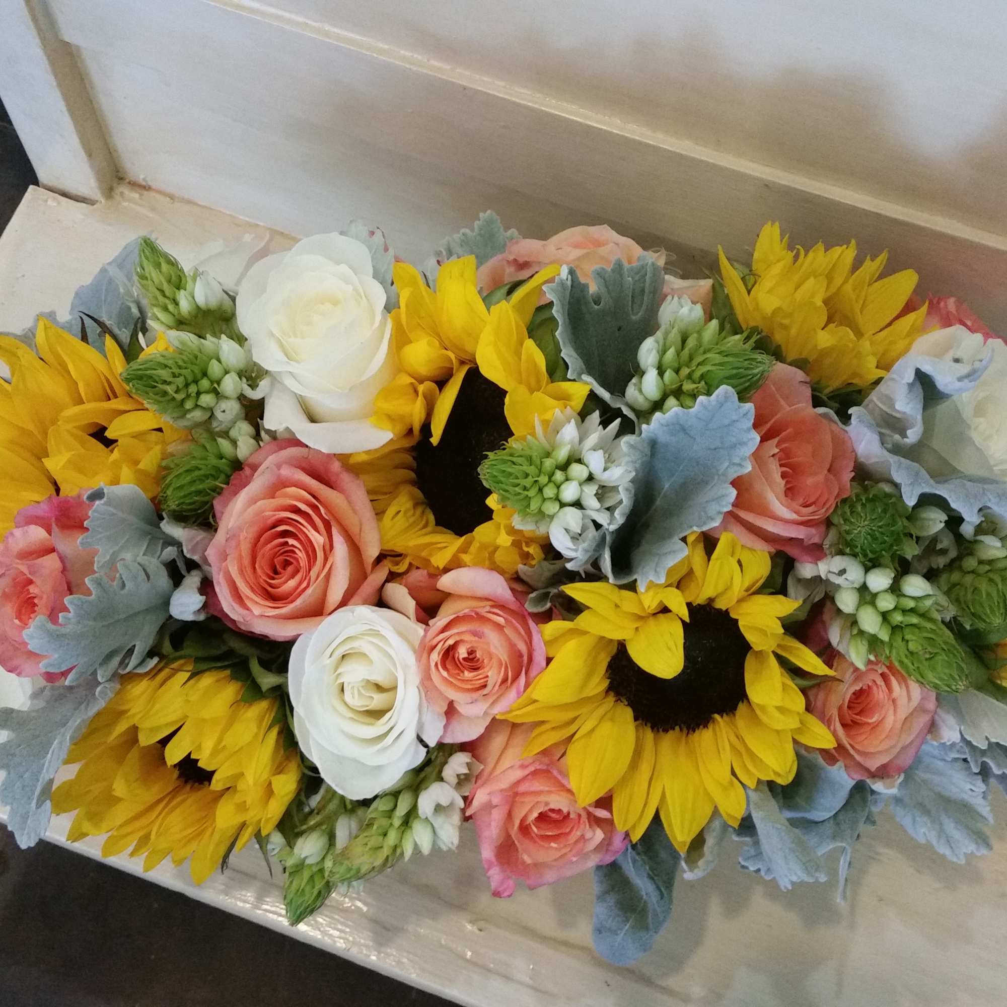 Low bouquet of sunflowers, roses, and white blooms on a table