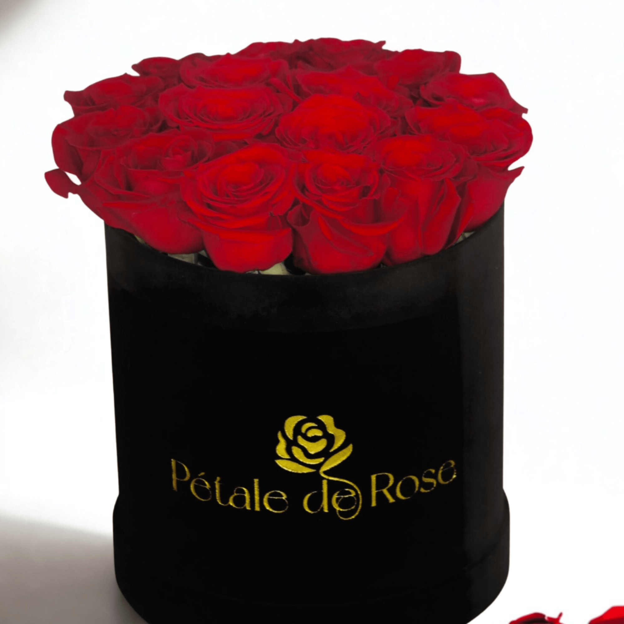 Round black hat box filled with tightly packed red roses with a gold logo on the front.