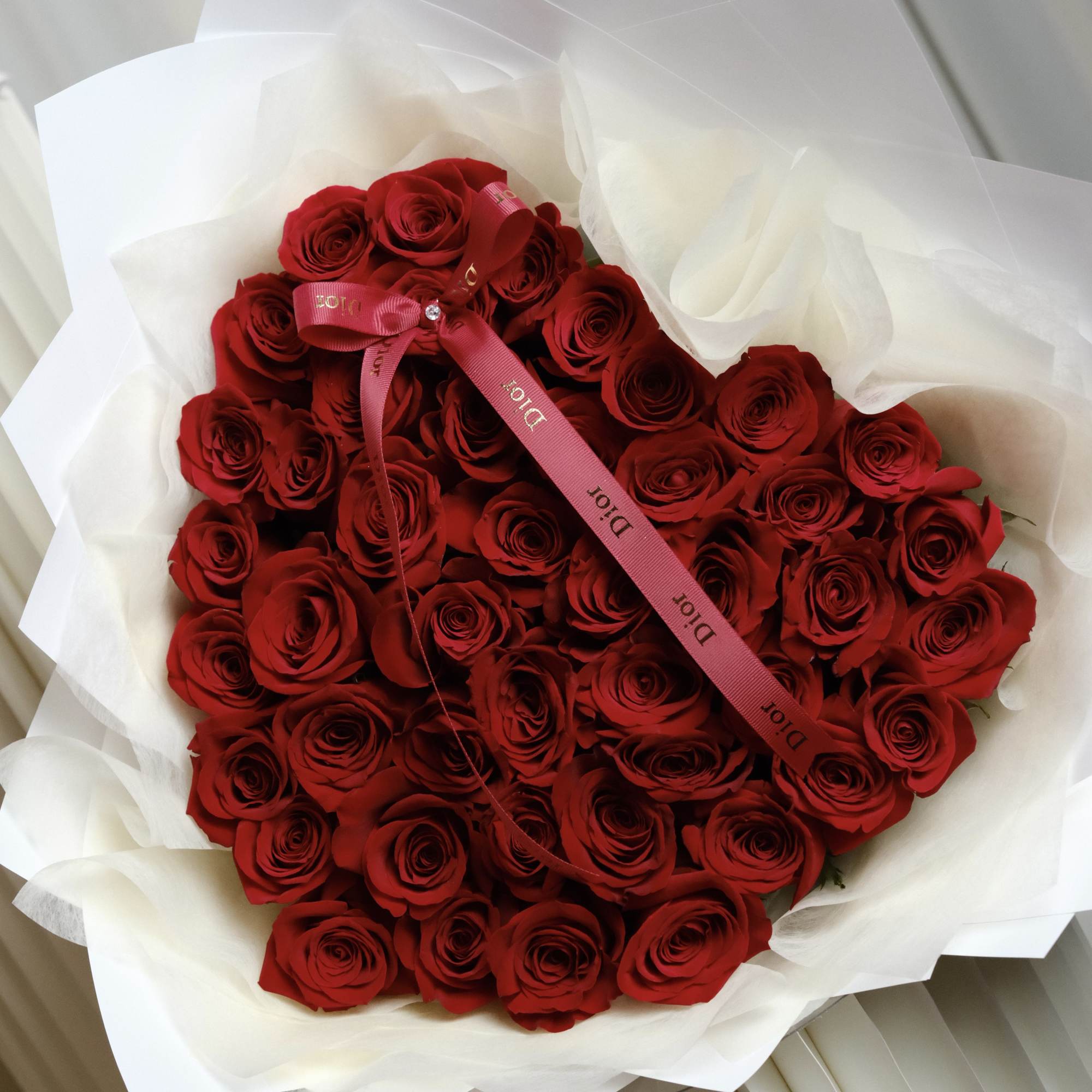 Large bouquet of red roses wrapped in white paper with a pink ribbon