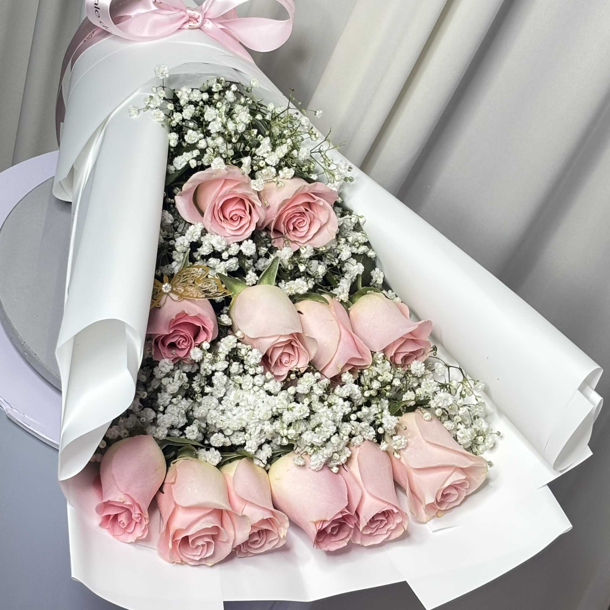 Bouquet of pink roses and white baby's breath wrapped in white paper with a pink ribbon