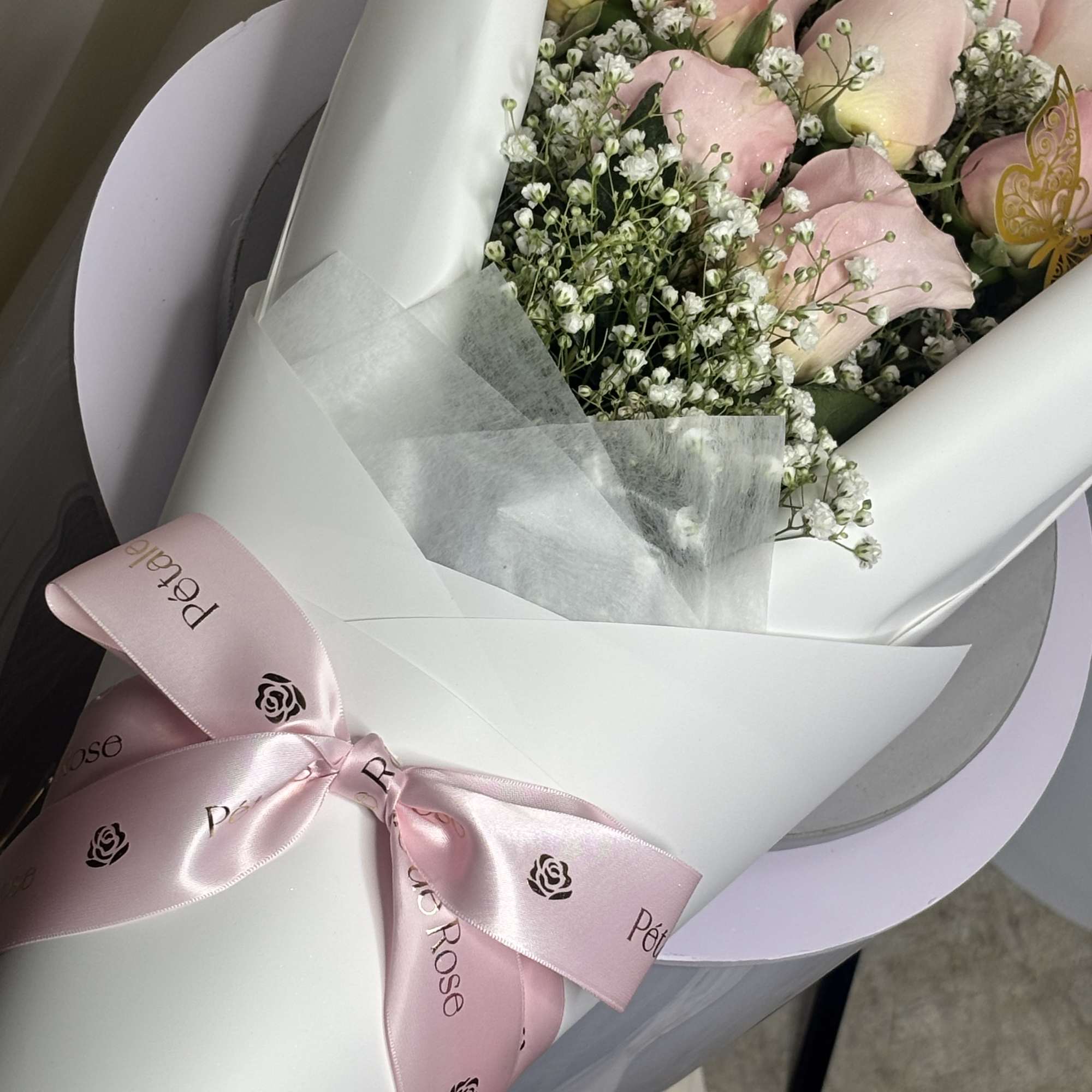 Bouquet of pale pink roses with baby's breath in white wrapping and a pink ribbon