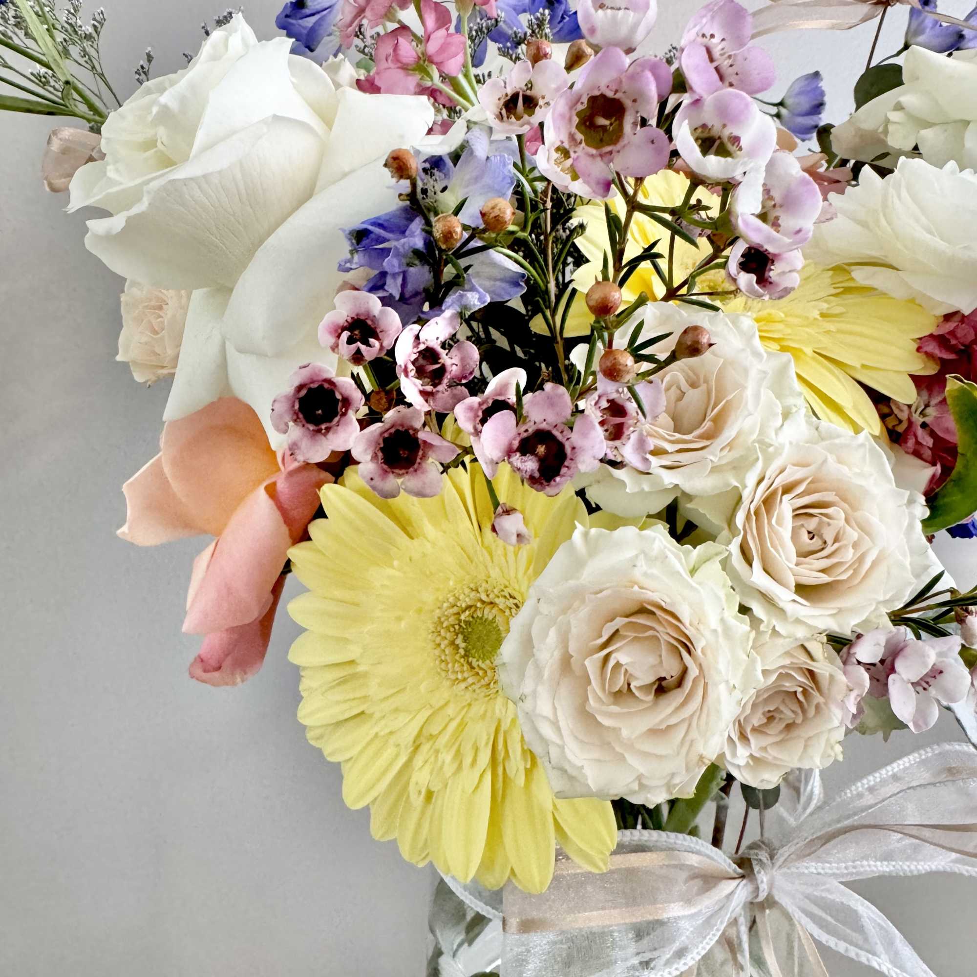 Mixed bouquet of roses, daisies, and pink blossoms in a glass vase with ribbon