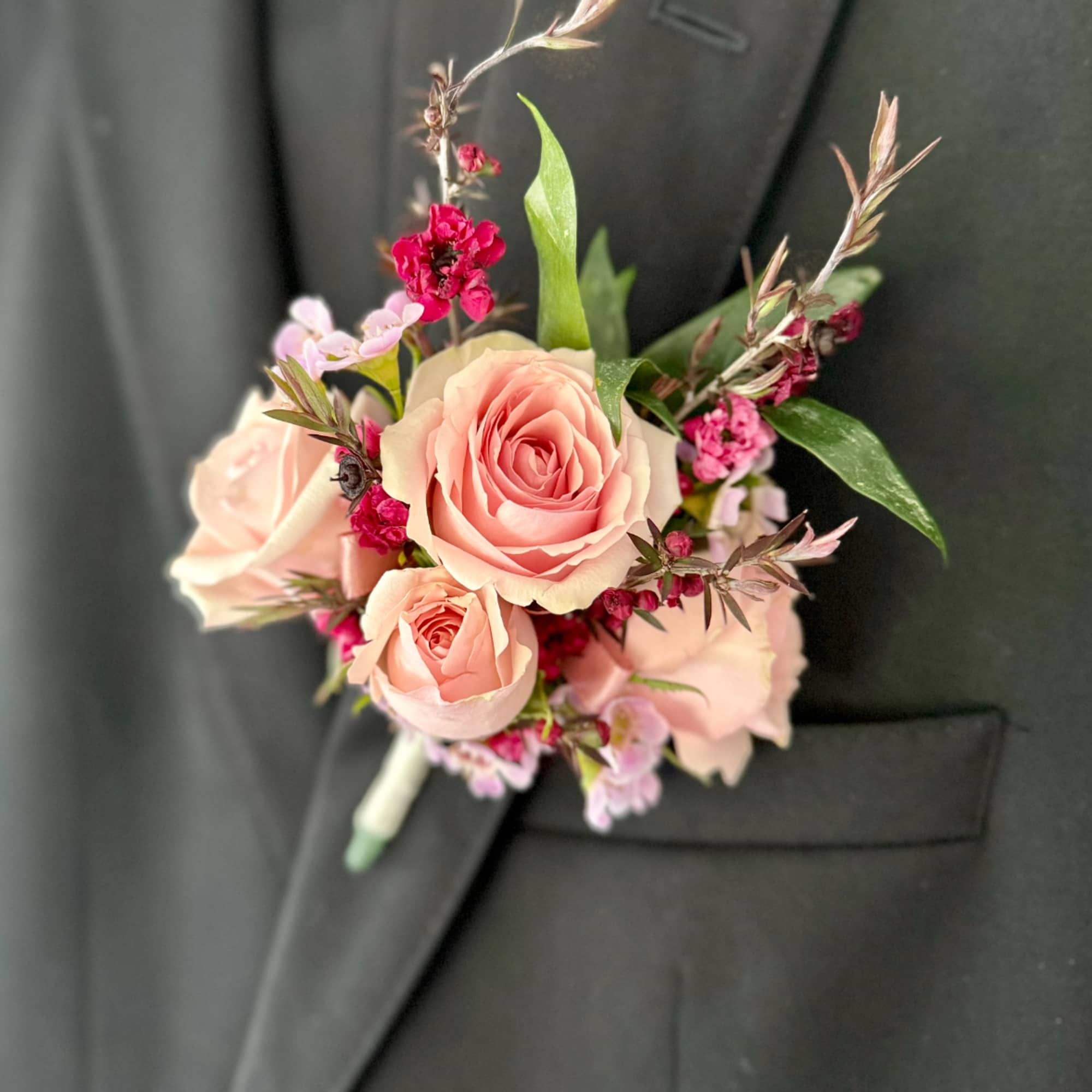 Pink rose boutonniere with small accent flowers on a dark suit lapel