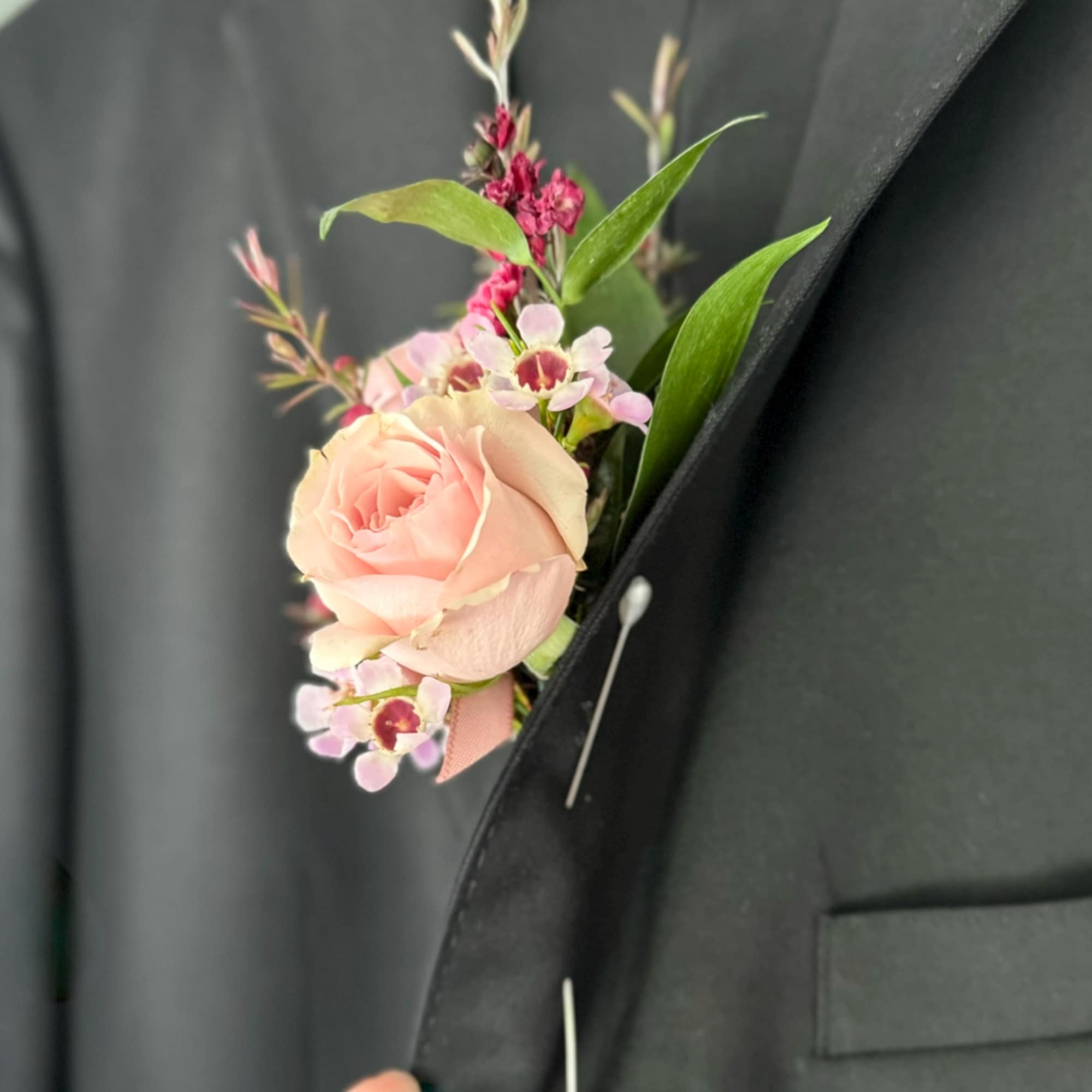 Pink rose boutonniere pinned to a black suit jacket