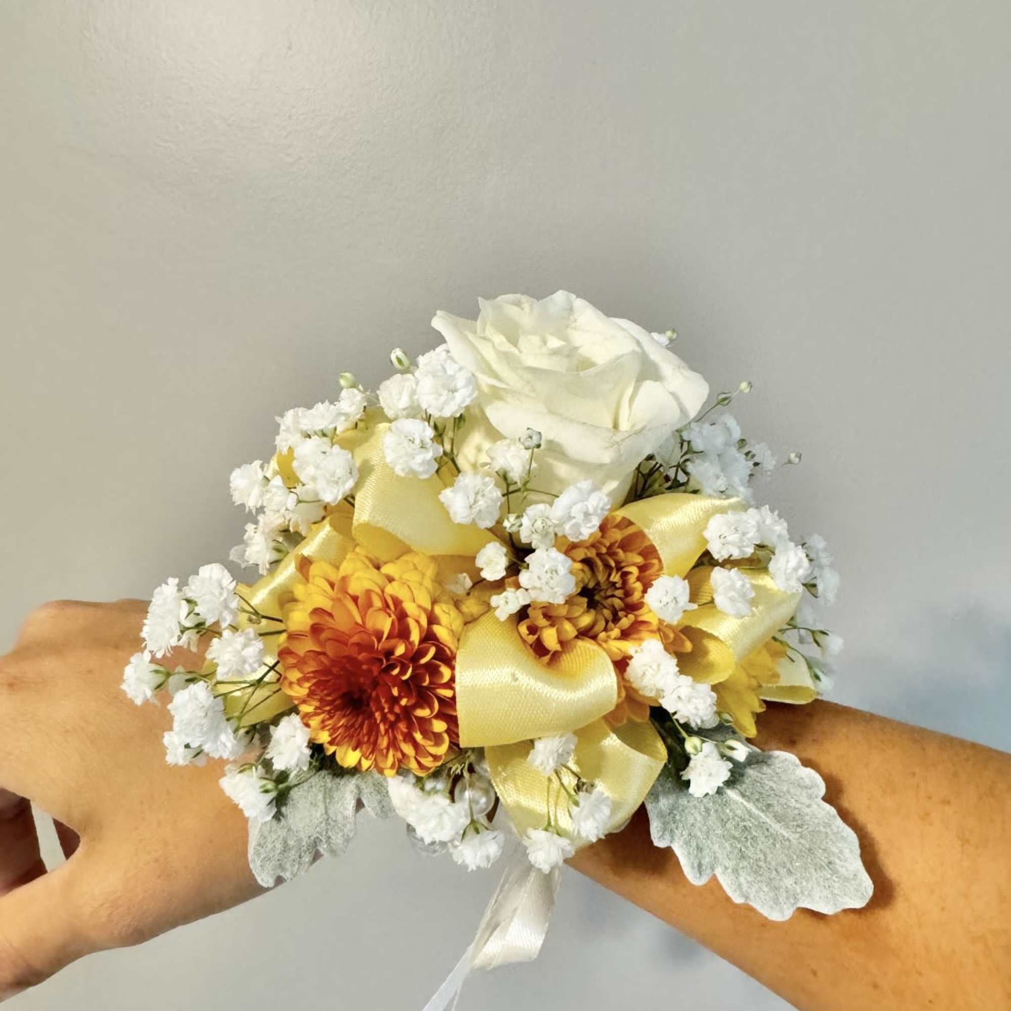 Corsage with white rose, yellow-orange blooms, and ribbon on a wrist