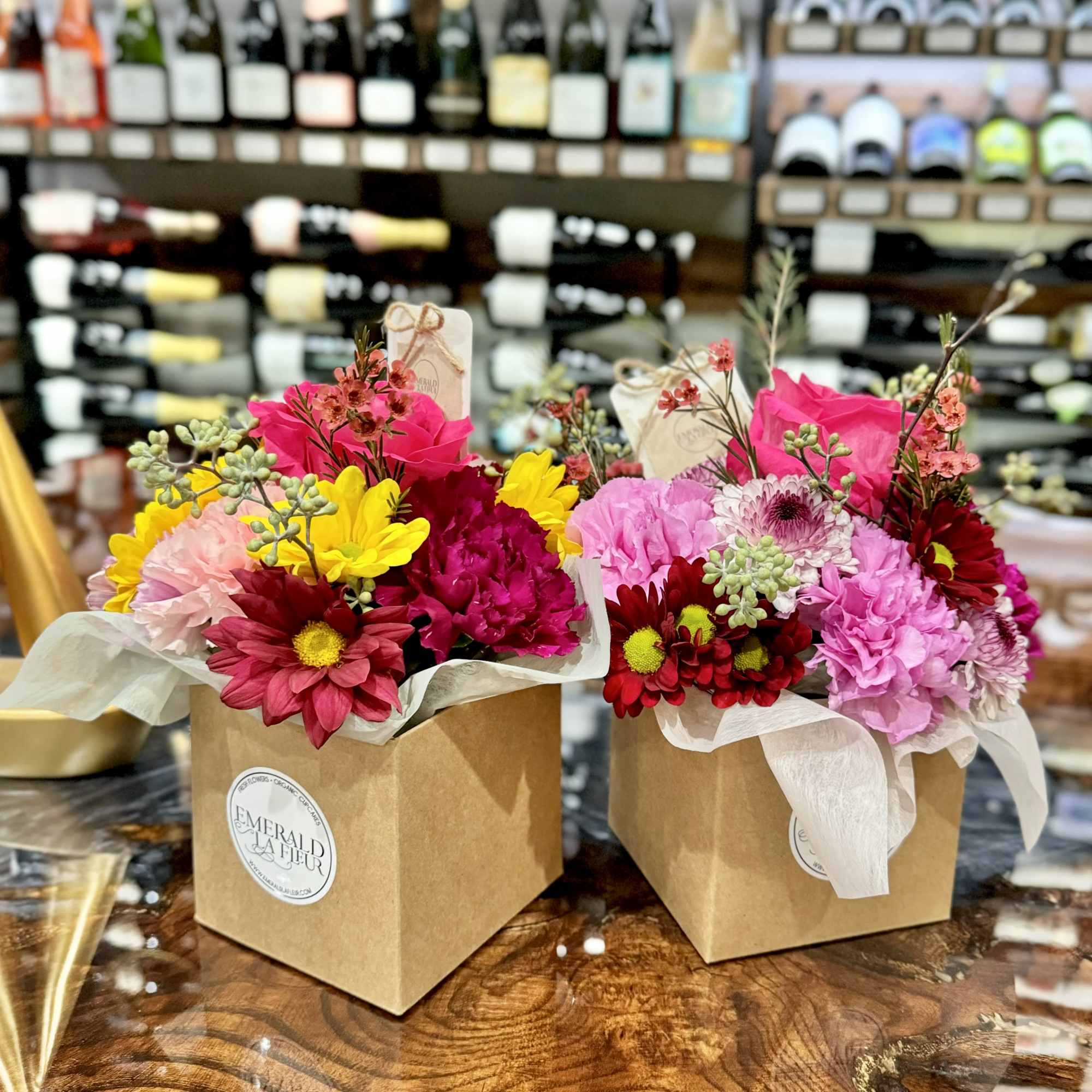 Two bright mixed flower arrangements in kraft boxes on a wooden table