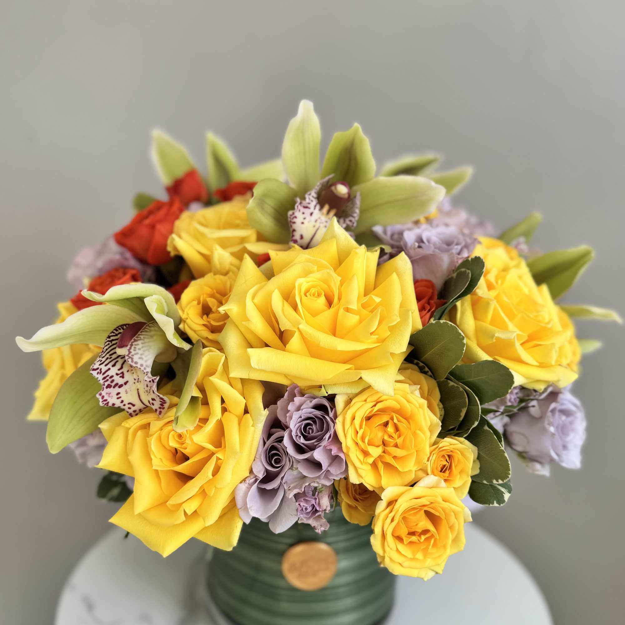 Yellow roses and orchids arranged in a green vase