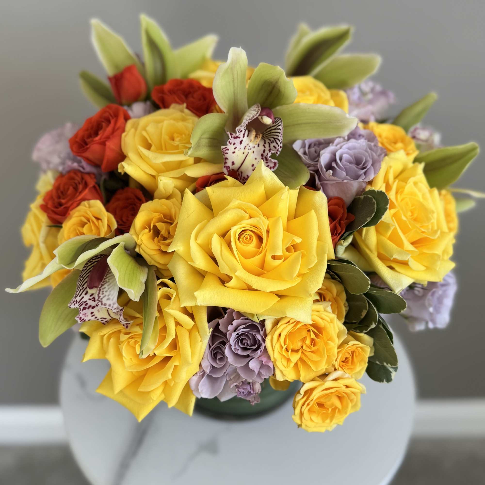 Bouquet of yellow, red, and lavender roses with green orchids in a vase