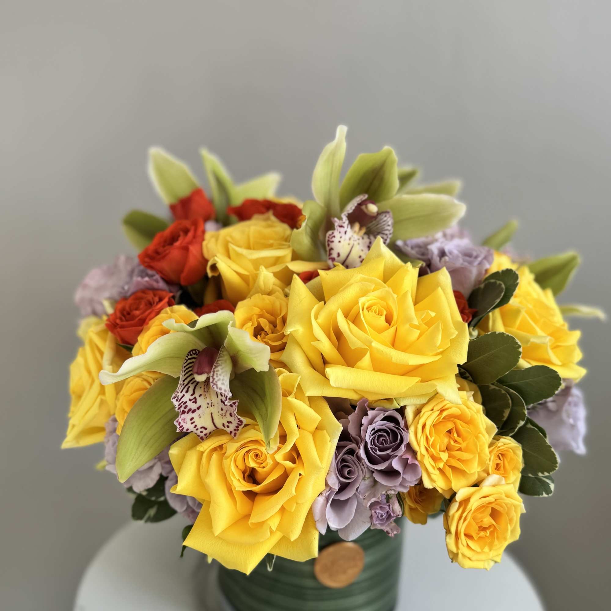 Yellow and red roses with orchids in a green vase
